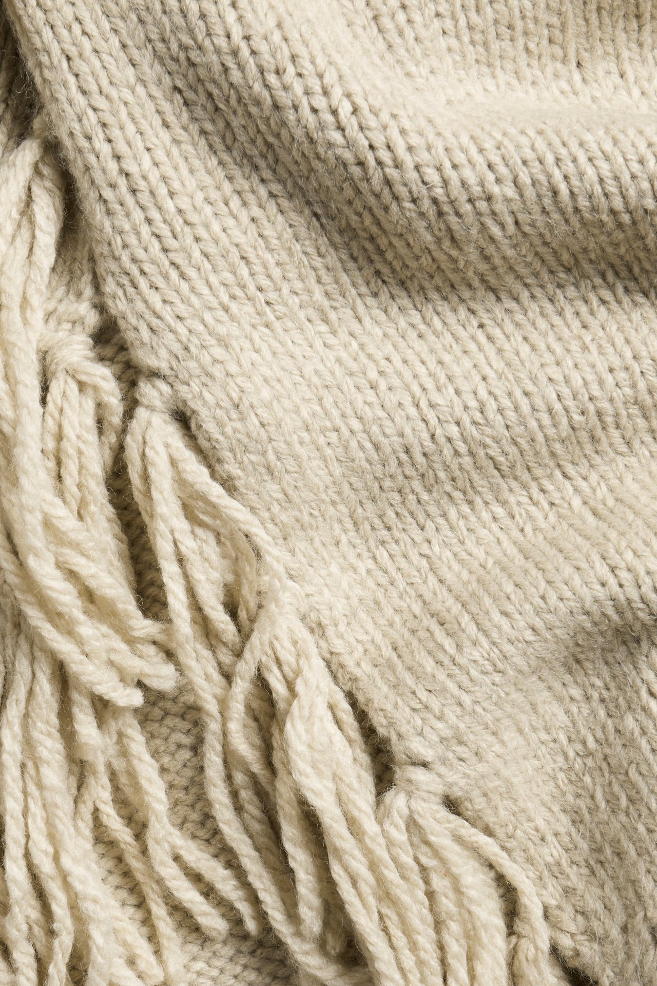 Zbliżenie beżowego melanżowego swetra z dzianiny z frędzlami.