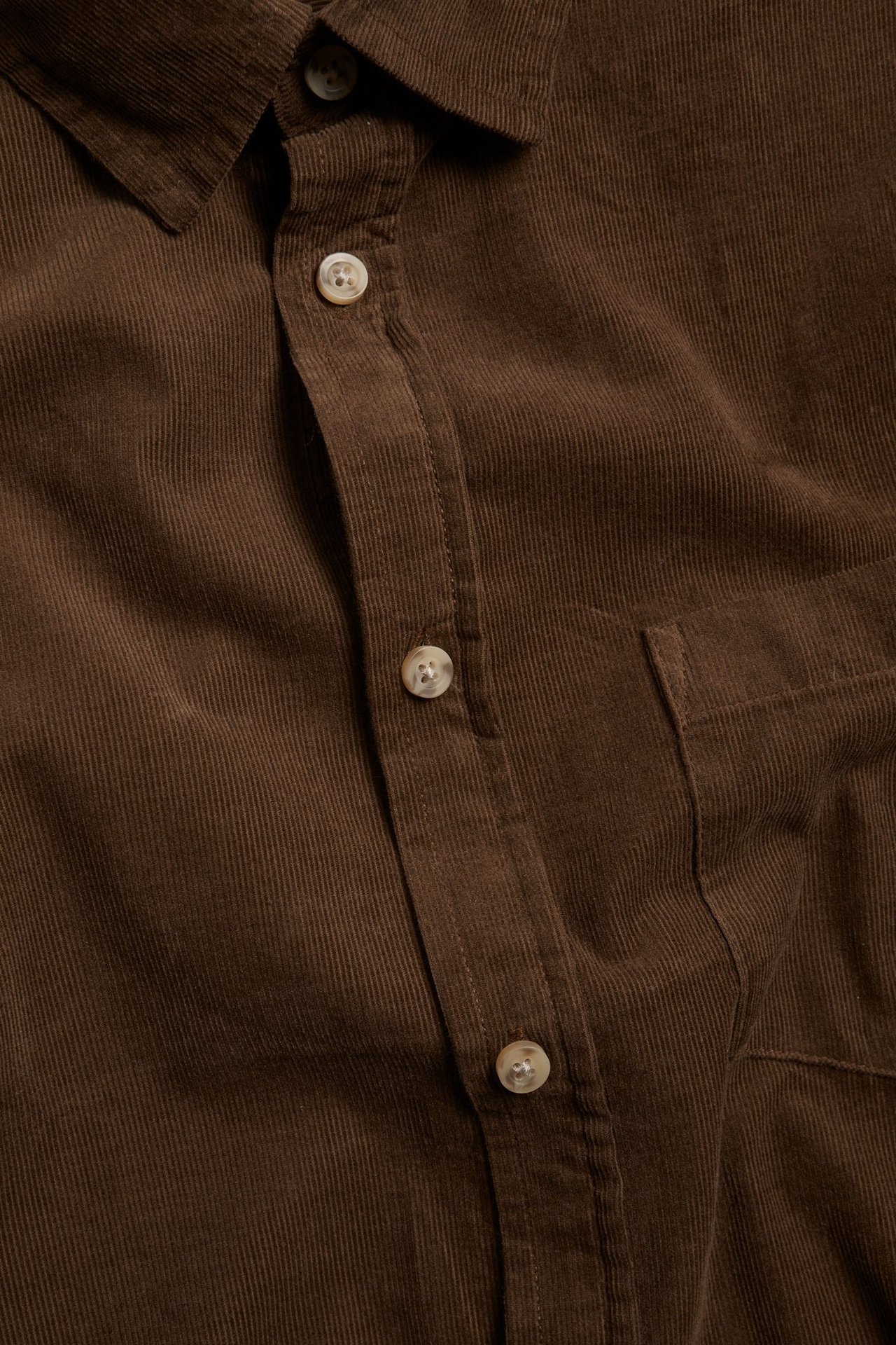 Zbliżenie brązowej męskiej koszuli sztruksowej z jasnymi guzikami i kieszenią na piersi.