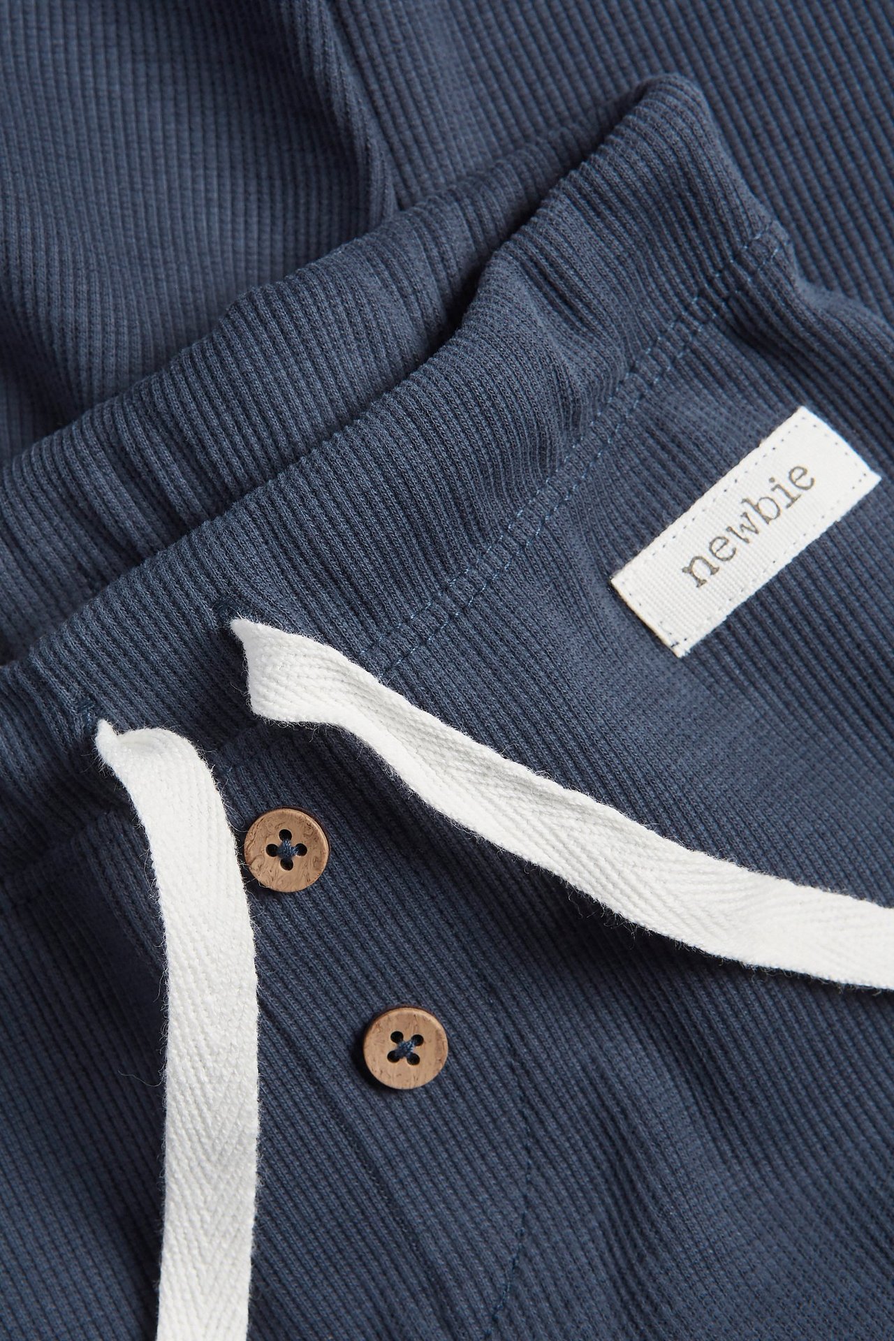 Zbliżenie na granatowe prążkowane legginsy z elastycznym pasem, białym sznurkiem i dwoma ozdobnymi drewnianymi guzikami.