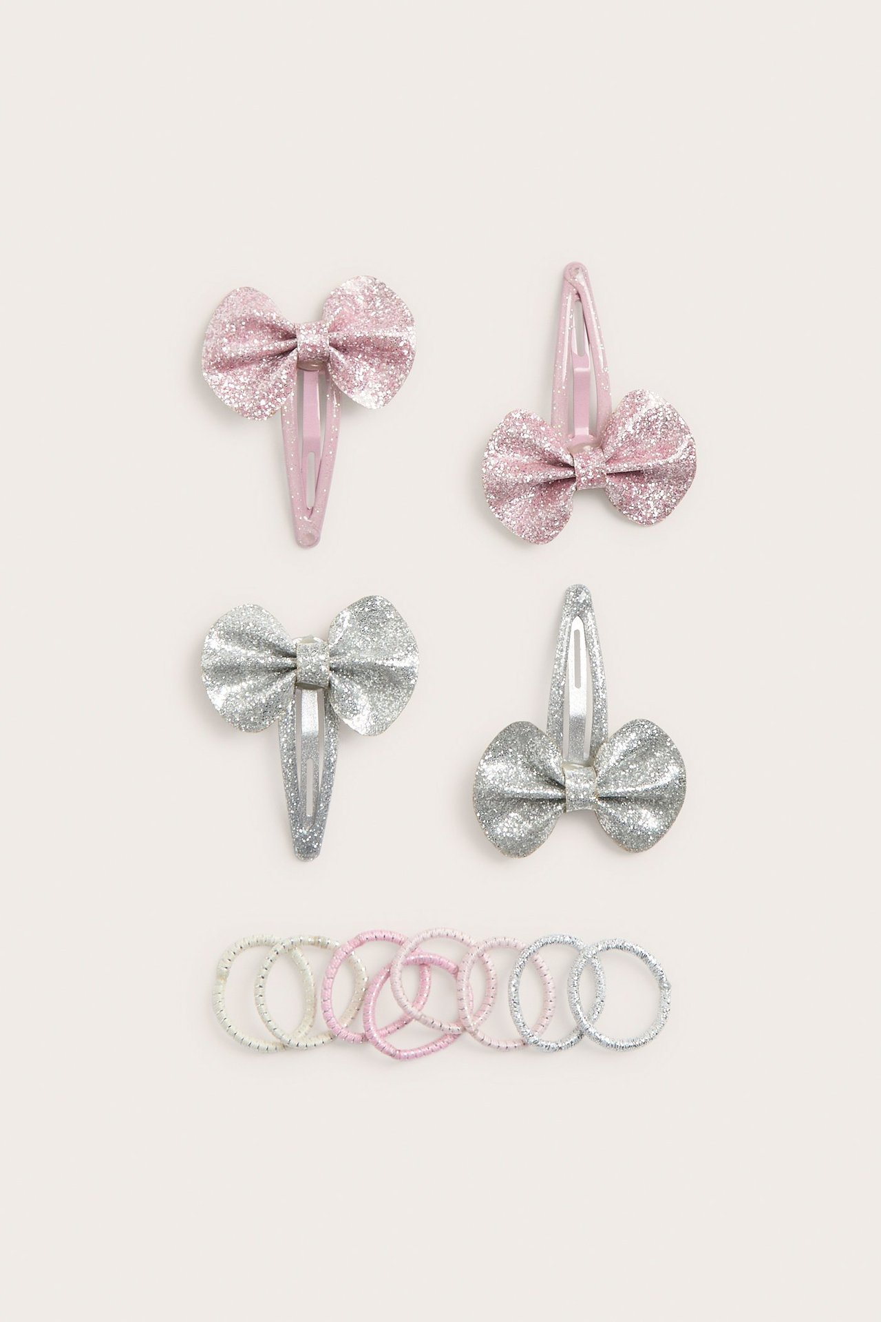 Widok z góry: Cztery brokatowe spinki z kokardkami w jasnym różu i srebrze, z pasującymi gumkami.