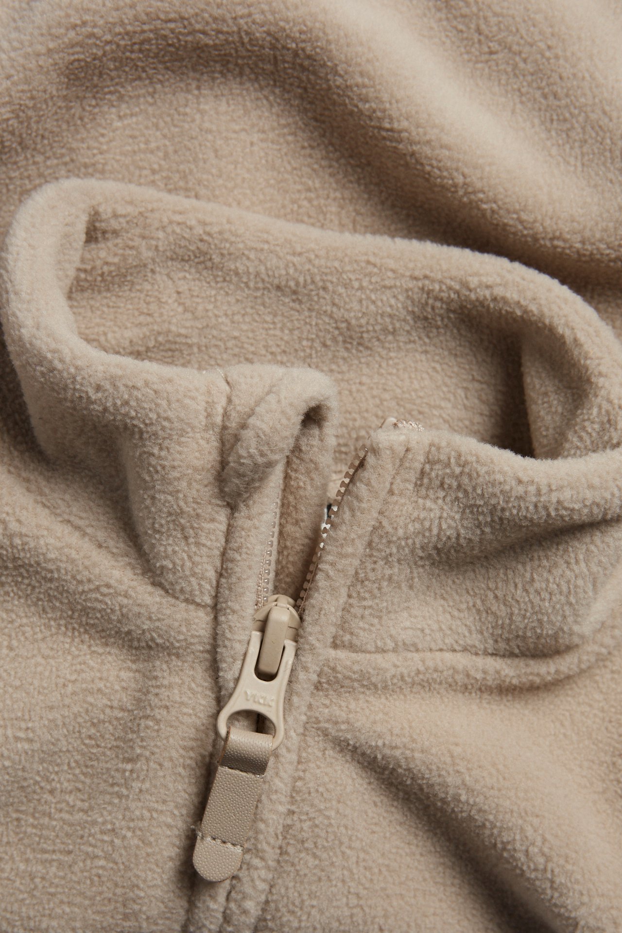 Närbild av en beige fleecejacka i återvunnen polyester med dragkedja och PU-dragare.