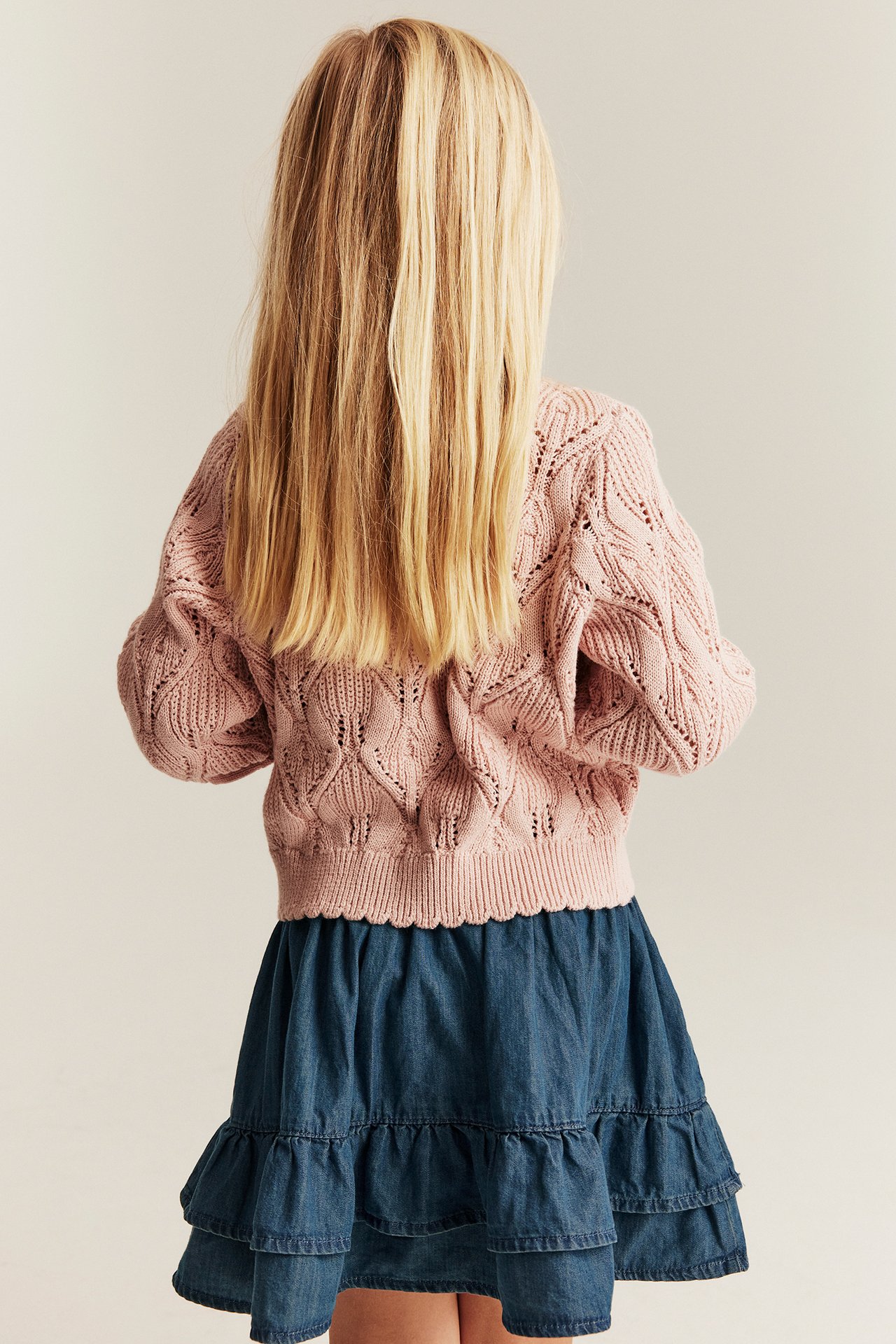 Z tyłu: dziecko w niebieskiej jeansowej spódniczce z falbanami i jasnoróżowym swetrze.