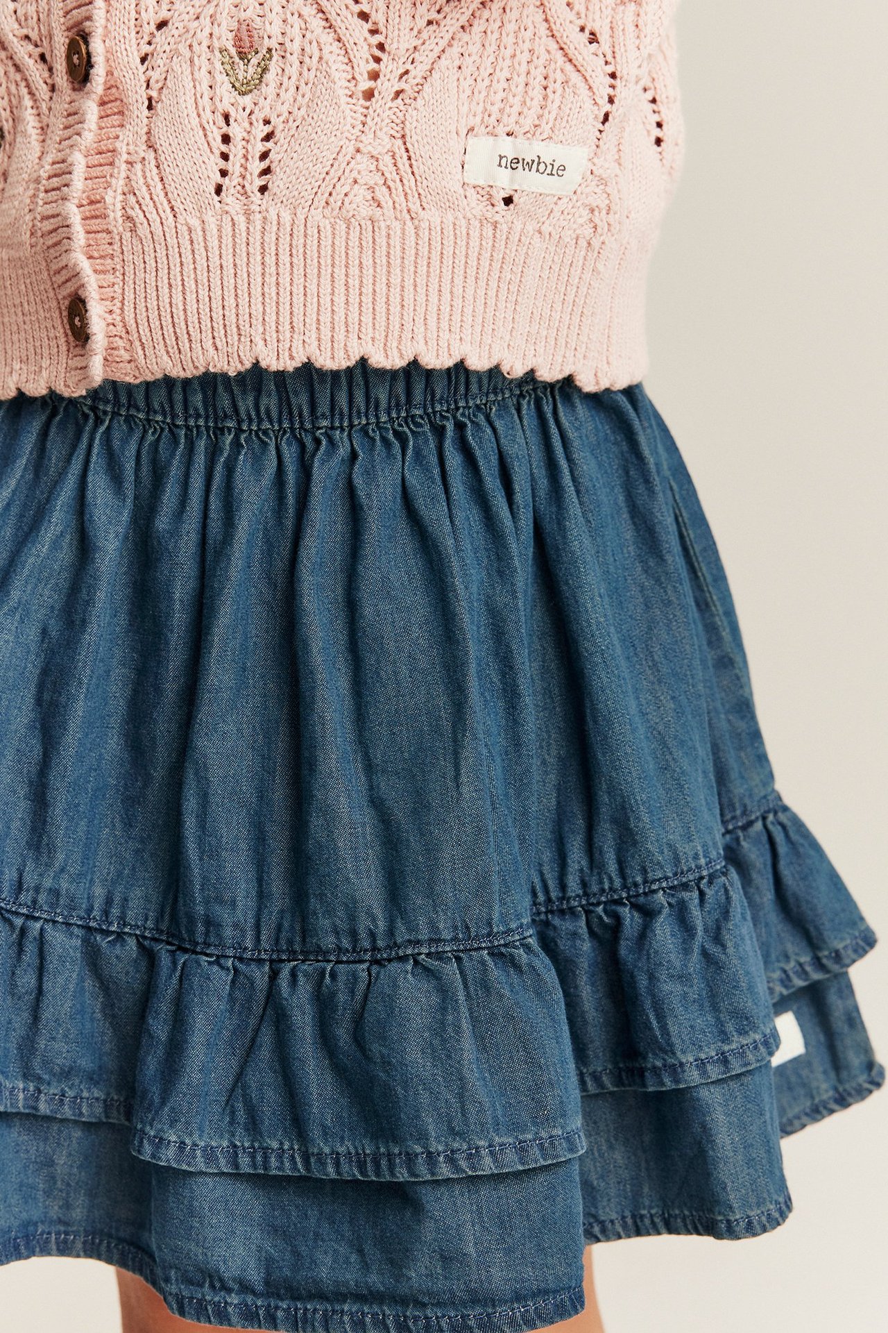 Zbliżenie na niebieską dżinsową spódnicę dziecięcą z gumką w pasie, falbankami i różowym swetrem.