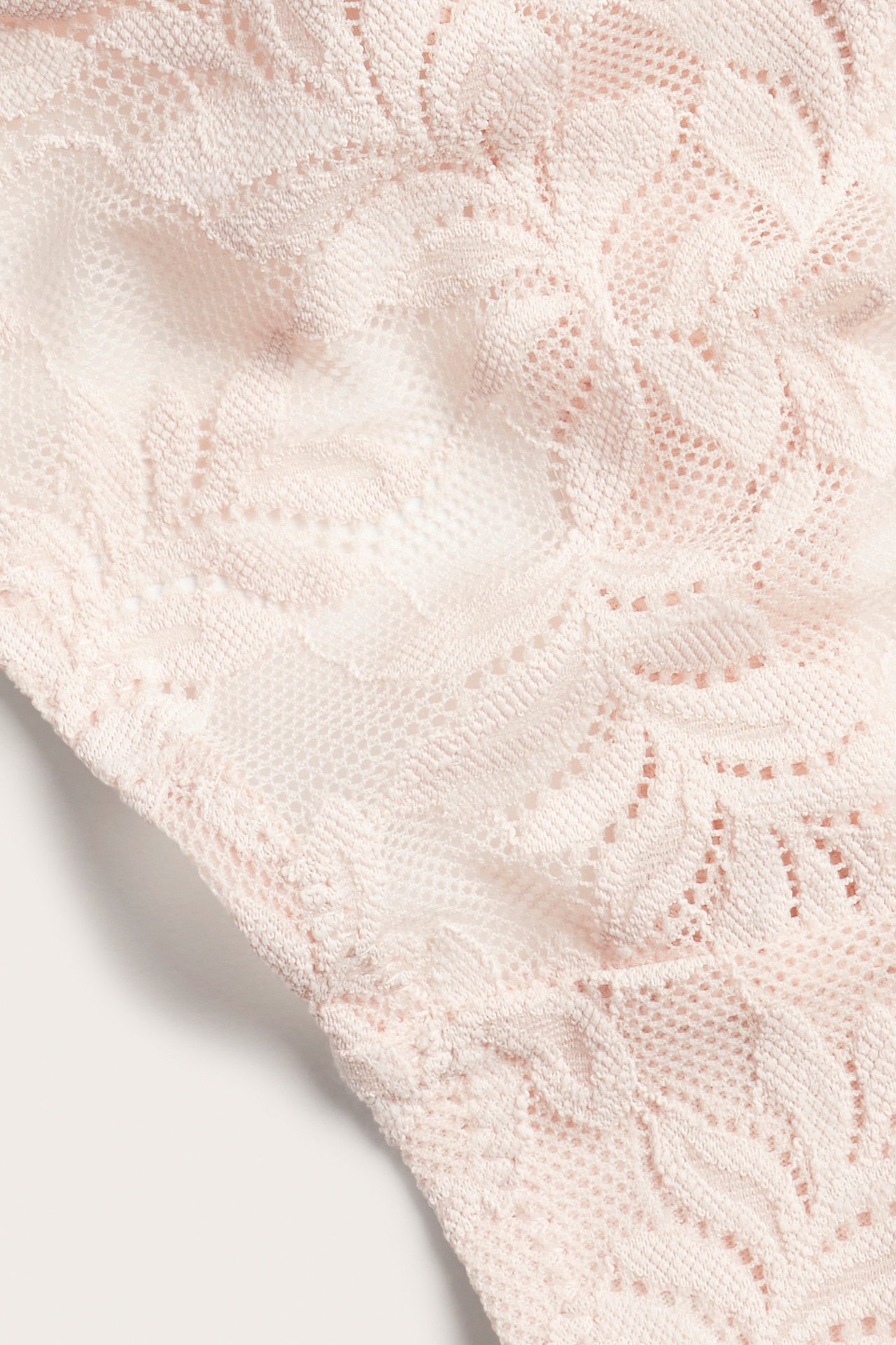 Zbliżenie jasnoróżowych koronkowych stringów z kwiatowym wzorem.