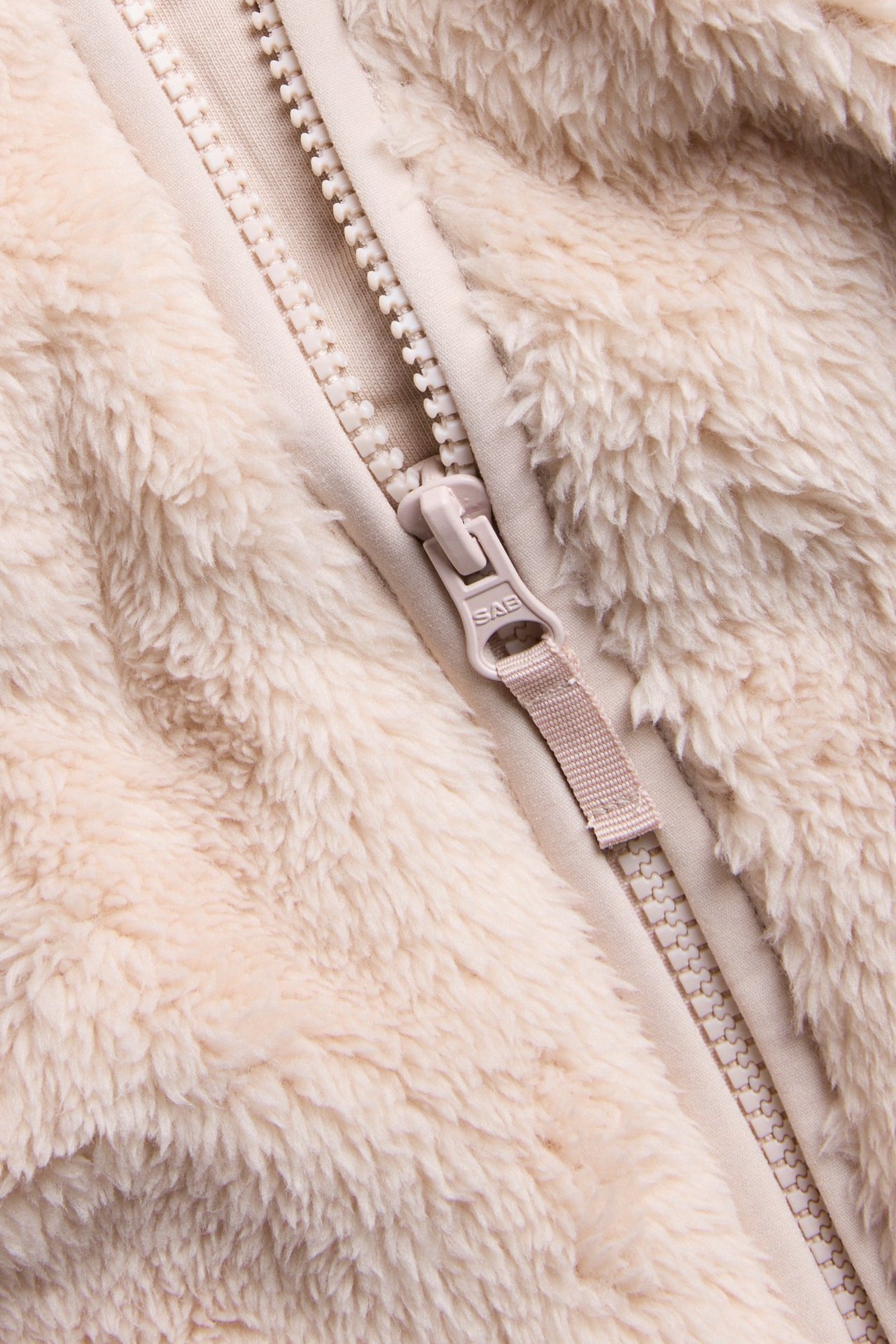 Zbliżenie na jasnoróżową, puszystą kurtkę polarową z pasującym zamkiem błyskawicznym.