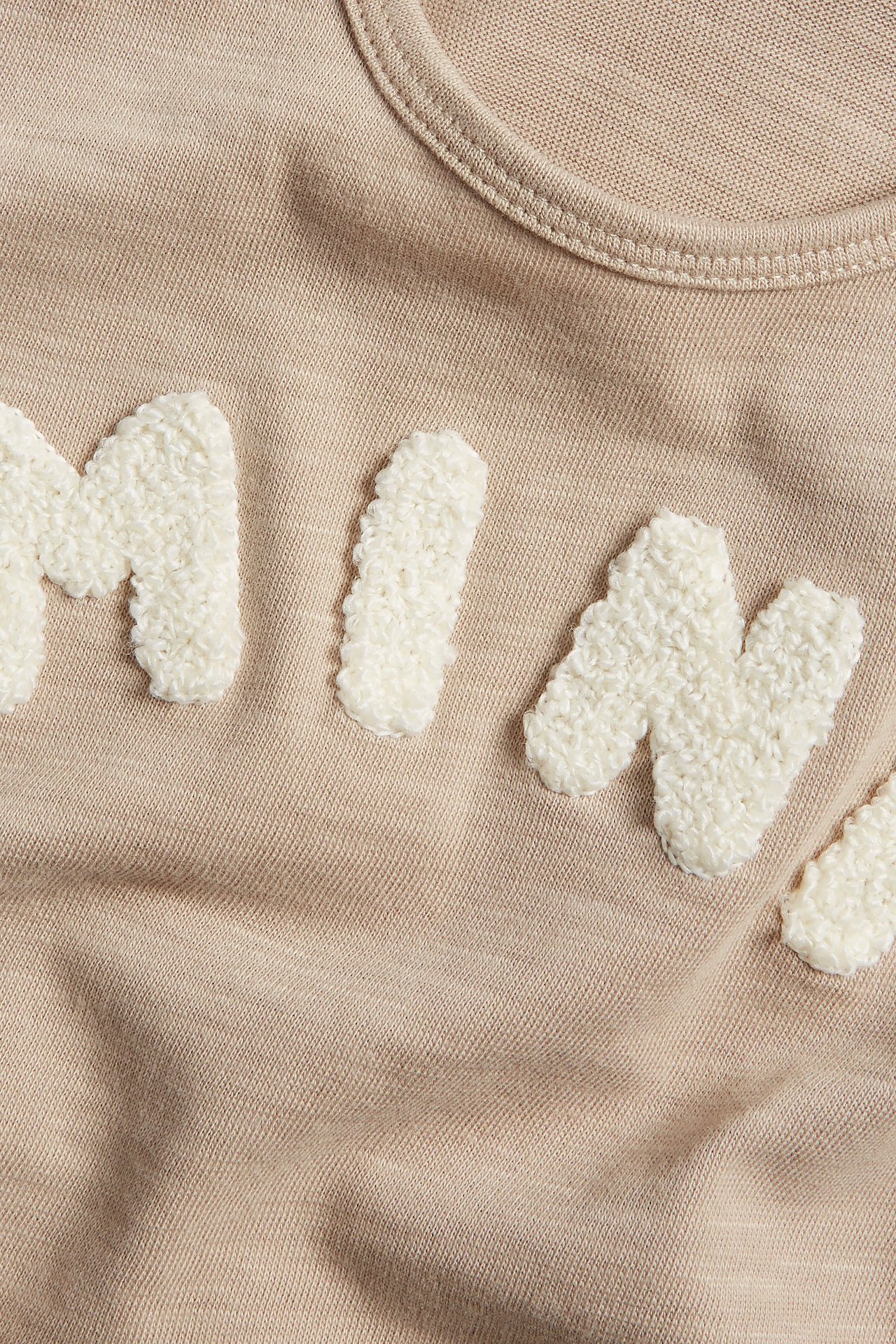 Zbliżenie beżowej bawełnianej koszulki z długim rękawem z białymi aplikacjami frotte.