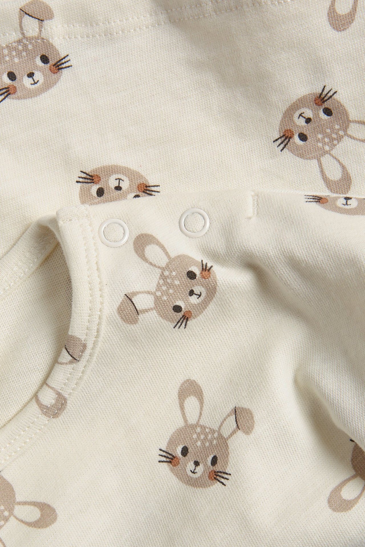 Zbliżenie na ecru bawełnianą bluzkę niemowlęcą z brązowym wzorem królików i białymi zatrzaskami.