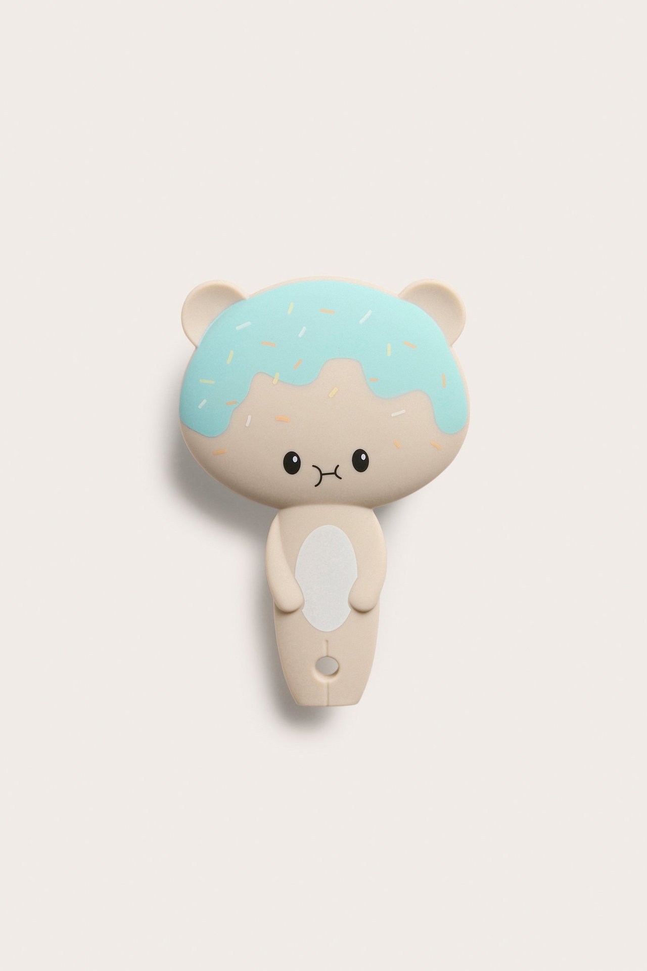 Etunäkymä: Vaaleanbeige muovinen hiusharja, joka on muotoiltu karhuksi vaaleansinisellä donitsikuorrutteella ja nonparelleilla.