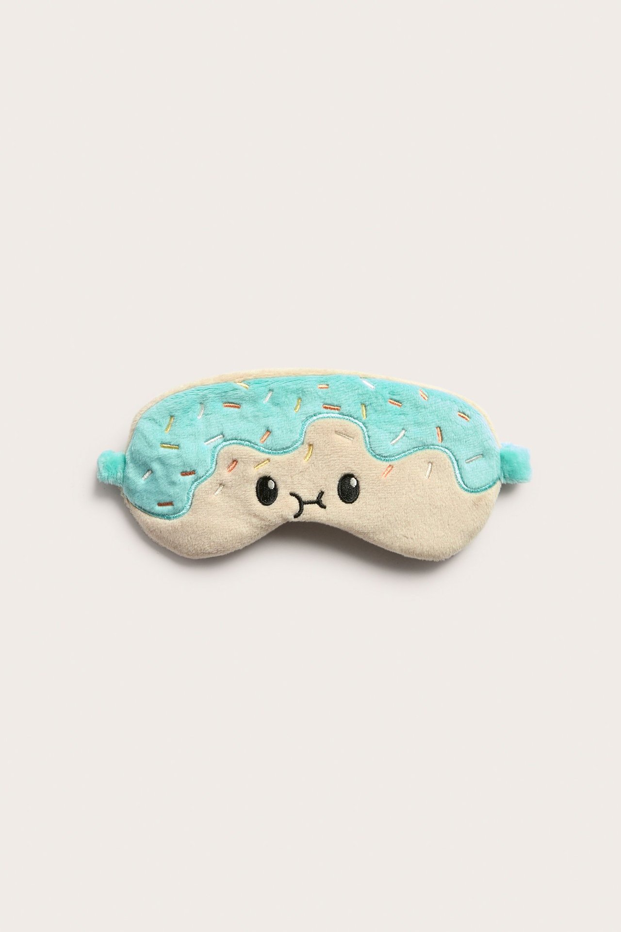 Etunäkymä: Vaaleanbeige veluurinen unimaski, donitsimuotoilu, sininen kuorrutus, nonparellit, kirjailtu naama.