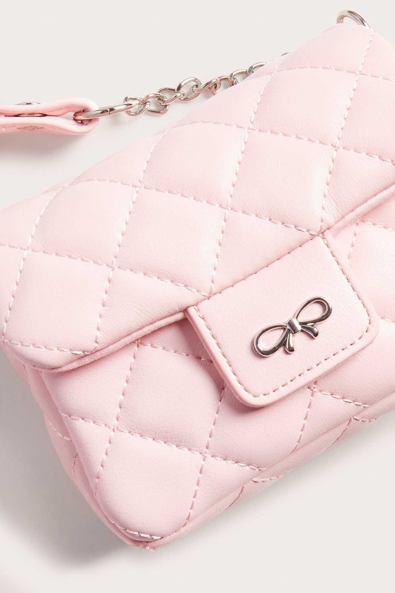 Lähikuva vaaleanpunaisesta tikatusta olkalaukusta, jossa on hopeinen rusetti läpässä ja ketjuhihna.