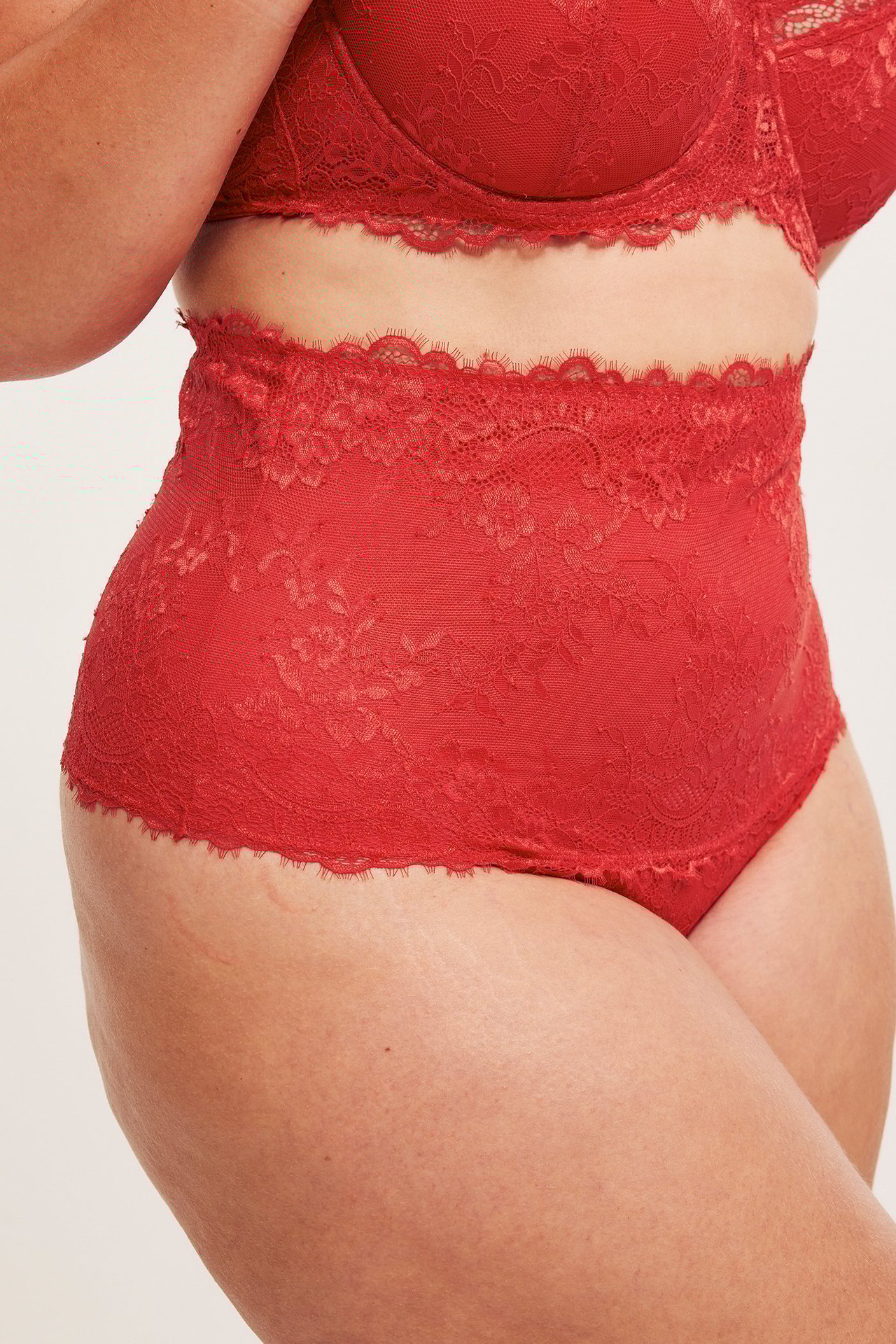 Närbild, sidovy av en kvinna i röd spetsstringtrosa med hög midja och matchande bh.