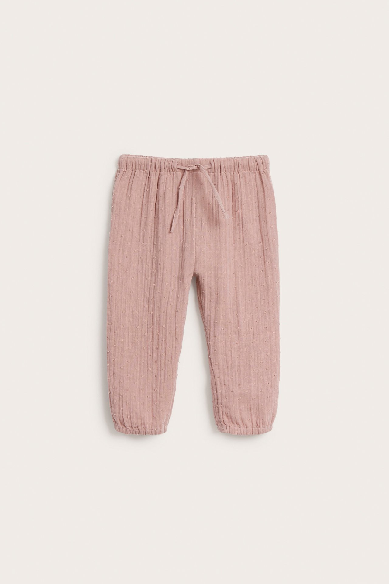 Frontvy av rosa vävda babybyxor med texturerad yta, resårmidja och dragsko.