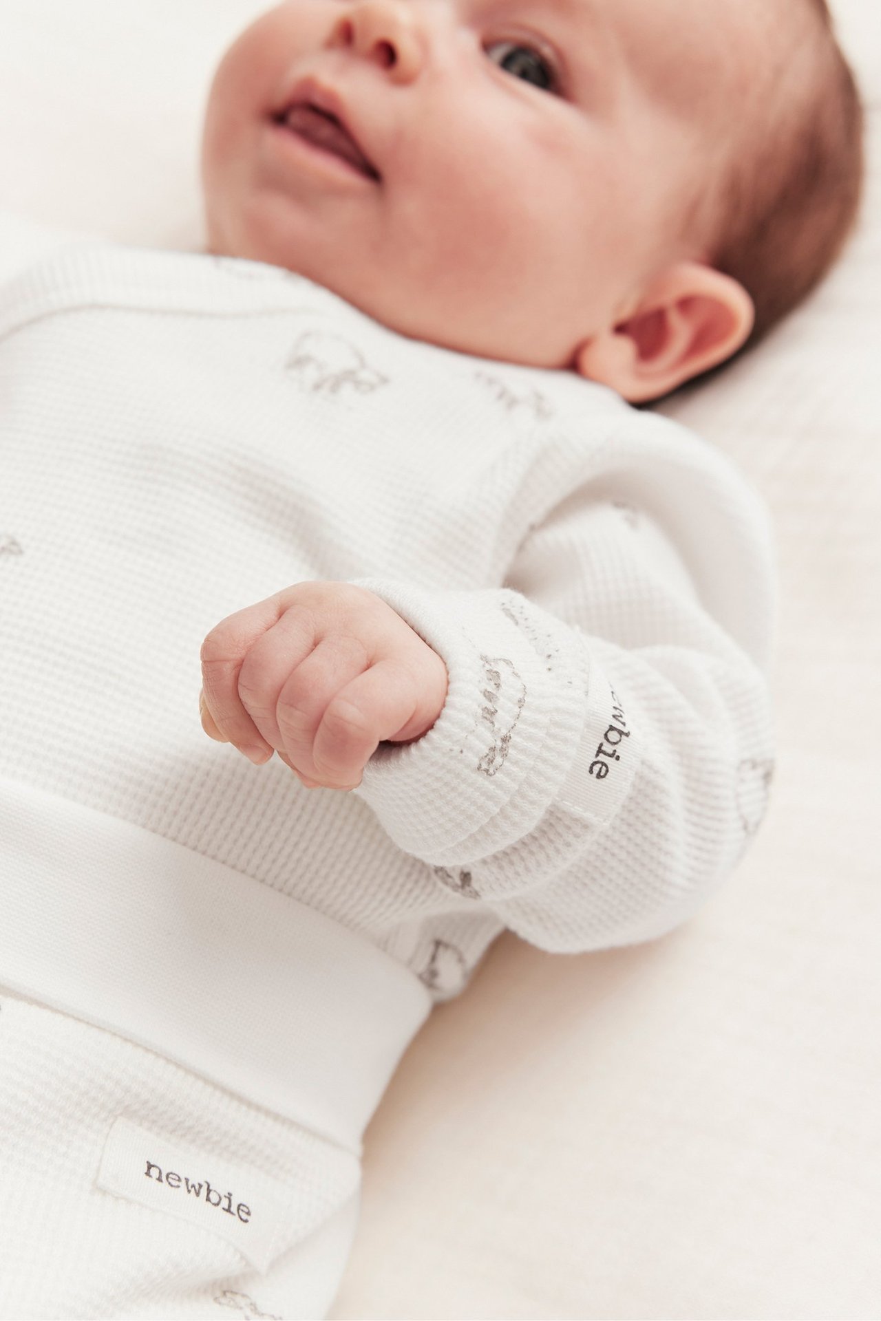 Närbild på baby i offwhite våfflad långärmad omlottbody med lammtryck.