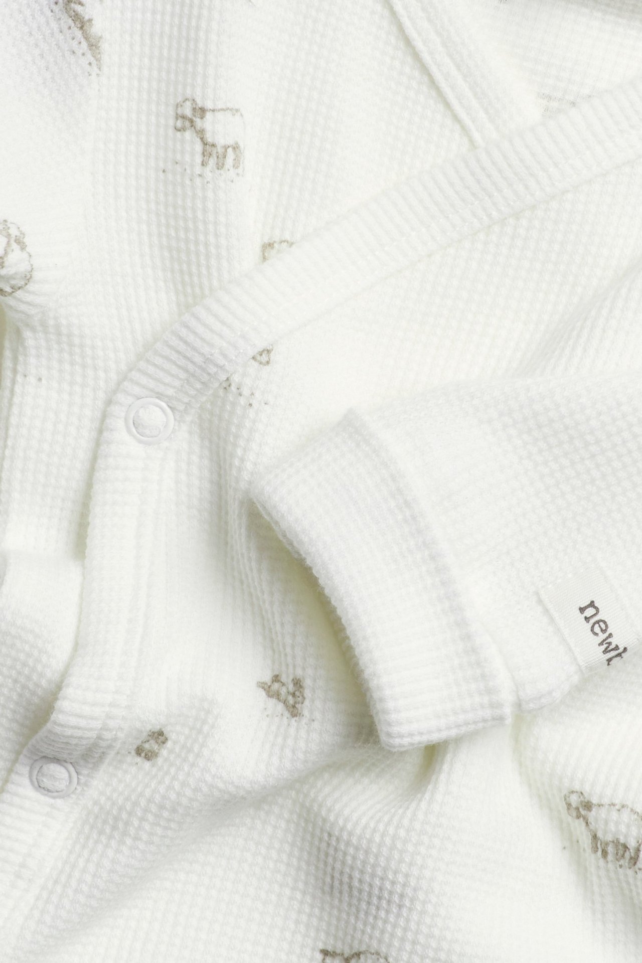 Zbliżenie na ecru body kopertowe dla niemowląt z waflowej dzianiny z nadrukiem owiec i zatrzaskami.