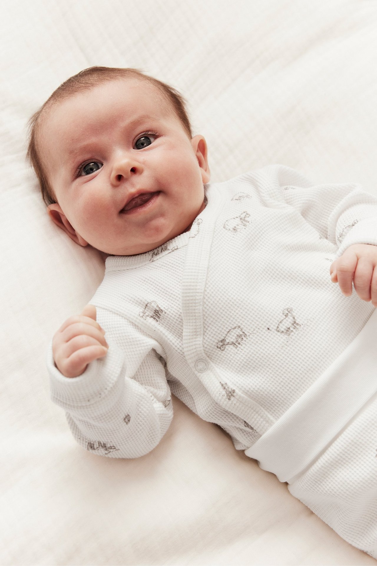 Frontvy, baby bär en offwhite våfflad omlottbody med lammtryck och tryckknappar.