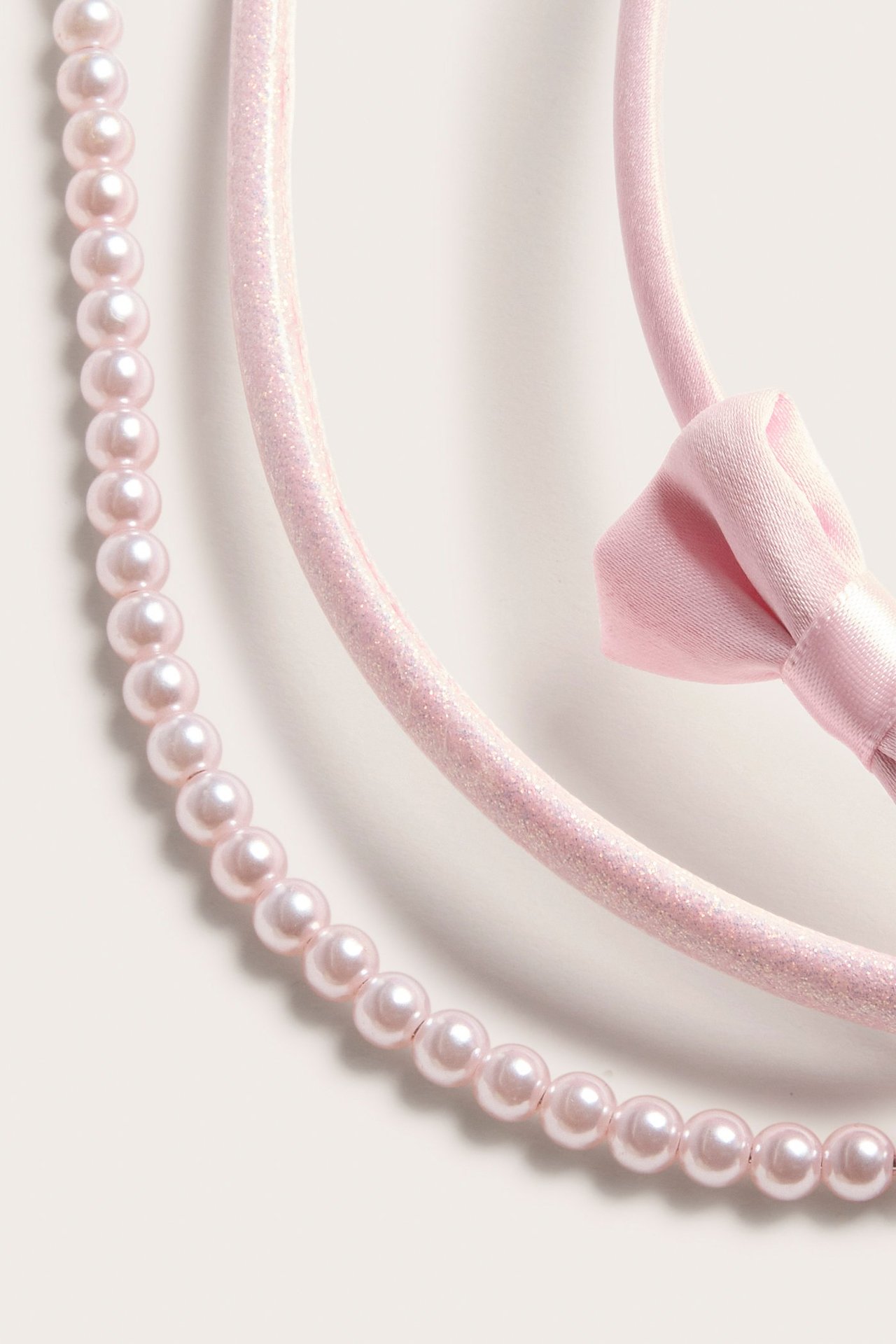 Lähikuva kolmesta vaaleanpunaisesta hiuspannasta: yksi helmillä, yksi kimalteleva ja yksi satiininen rusetilla.