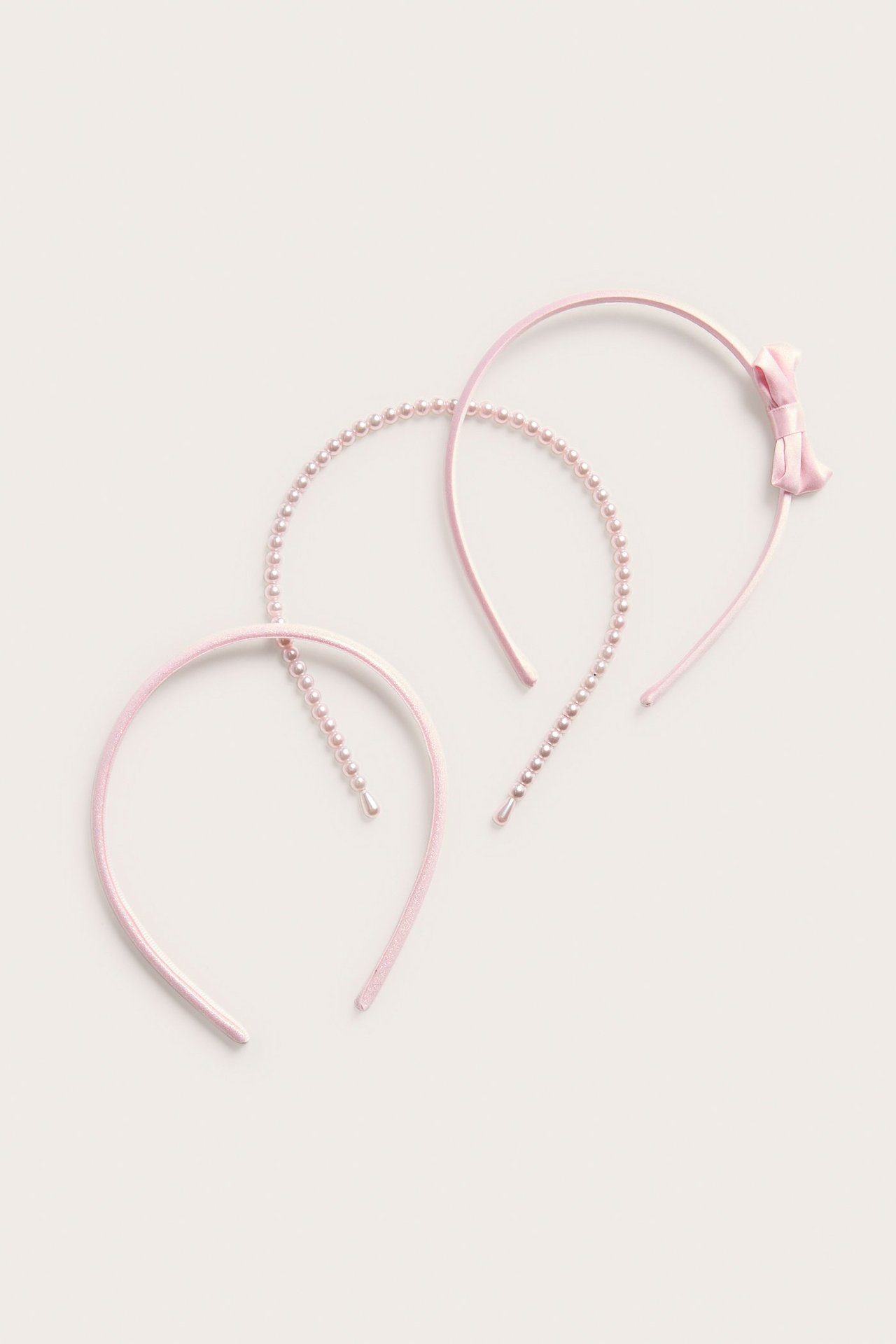 Ylhäältä: kolme vaaleanpunaista hiuspantaa; yksi rusetilla, yksi helmillä ja yksi yksivärinen.