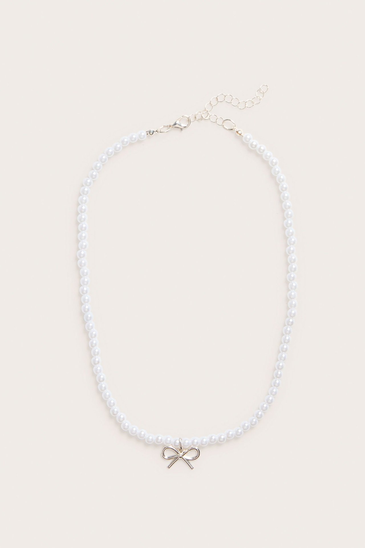 Ylhäältä kuvattu valkoinen helmikaulakoru, jossa hopeanvärinen rusettiriipus ja papukaijalukko.