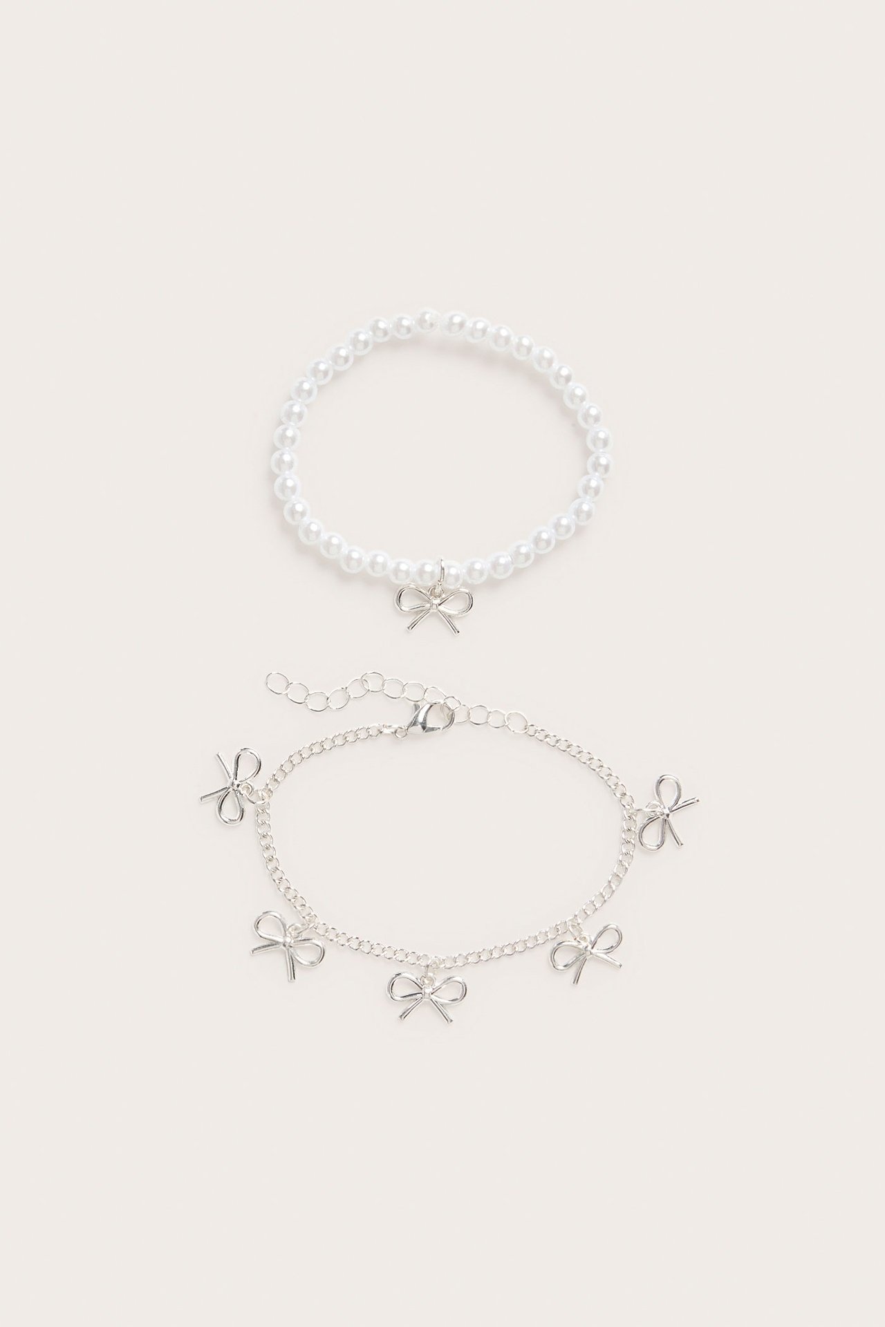 Widok z góry: biała perłowa bransoletka ze srebrną kokardką i srebrna bransoletka z łańcuszkiem z kokardkami.