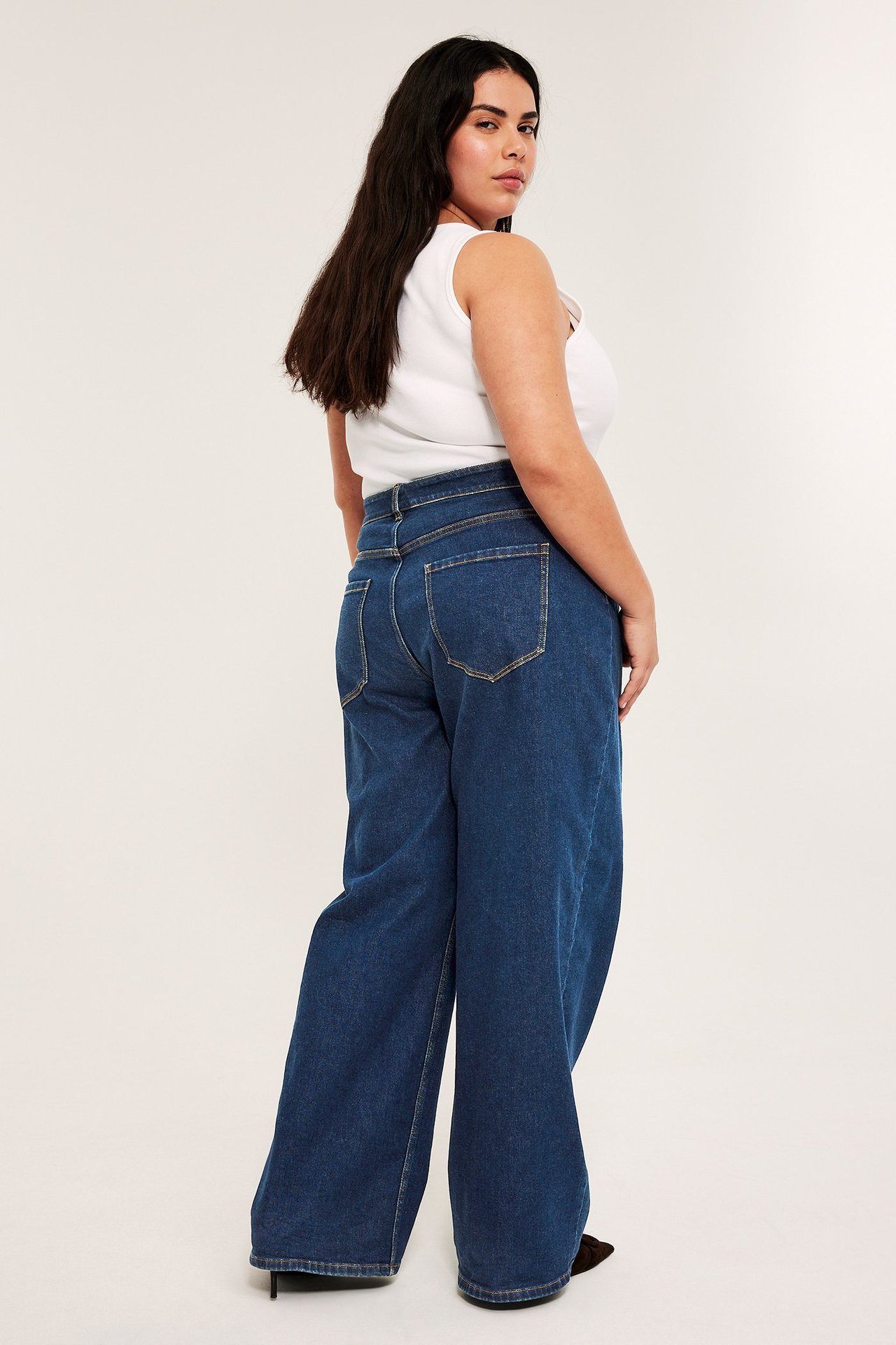 Widok z tyłu kobiety w szerokich granatowych jeansach z wysokim stanem i białym topie.