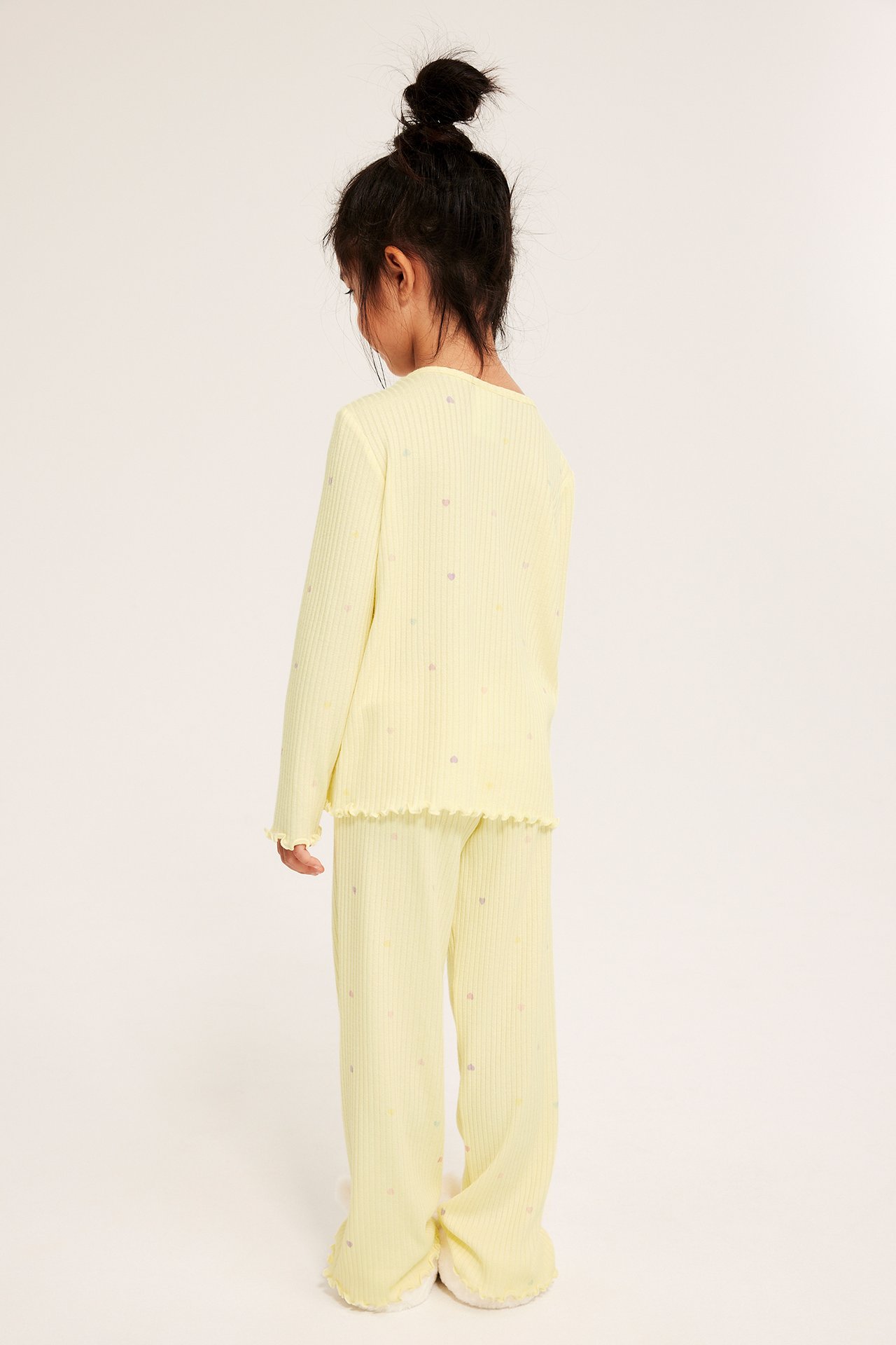 Bakifrån: Kid i ljusgul ribbad pyjamas med volangkanter och små hjärtan.
