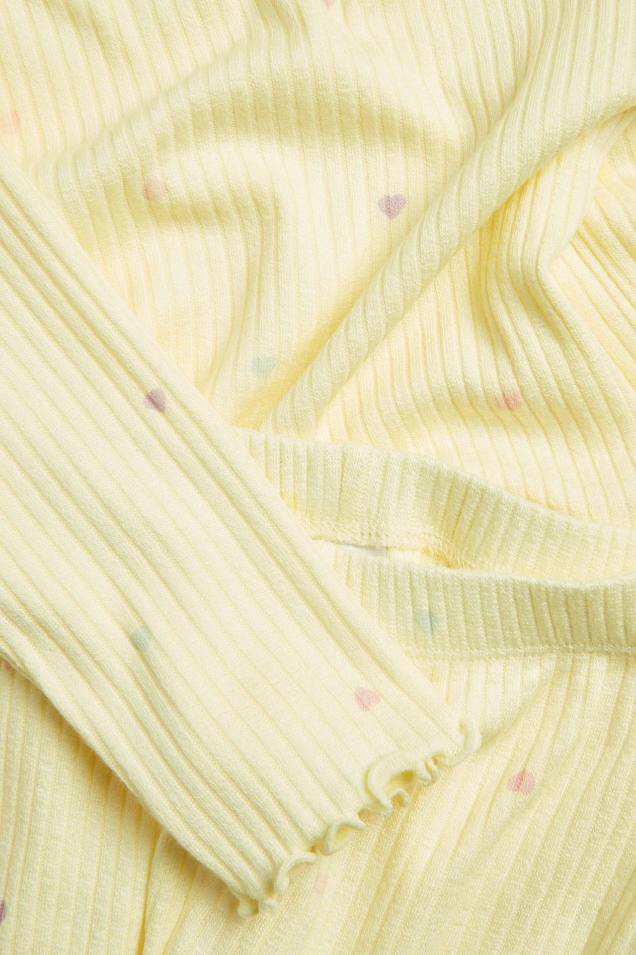 Zbliżenie na jasnożółtą prążkowaną piżamę dziecięcą z falbankami i wzorem w pastelowe serca.