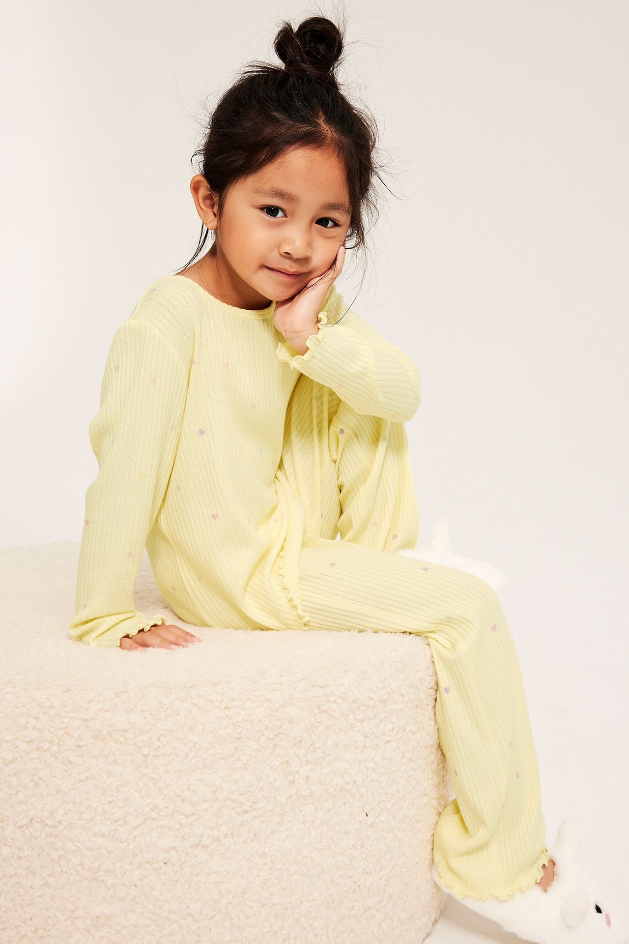 Dziecko w jasnożółtej prążkowanej piżamie w serca, z falbankami i białymi króliczkowymi kapciami.