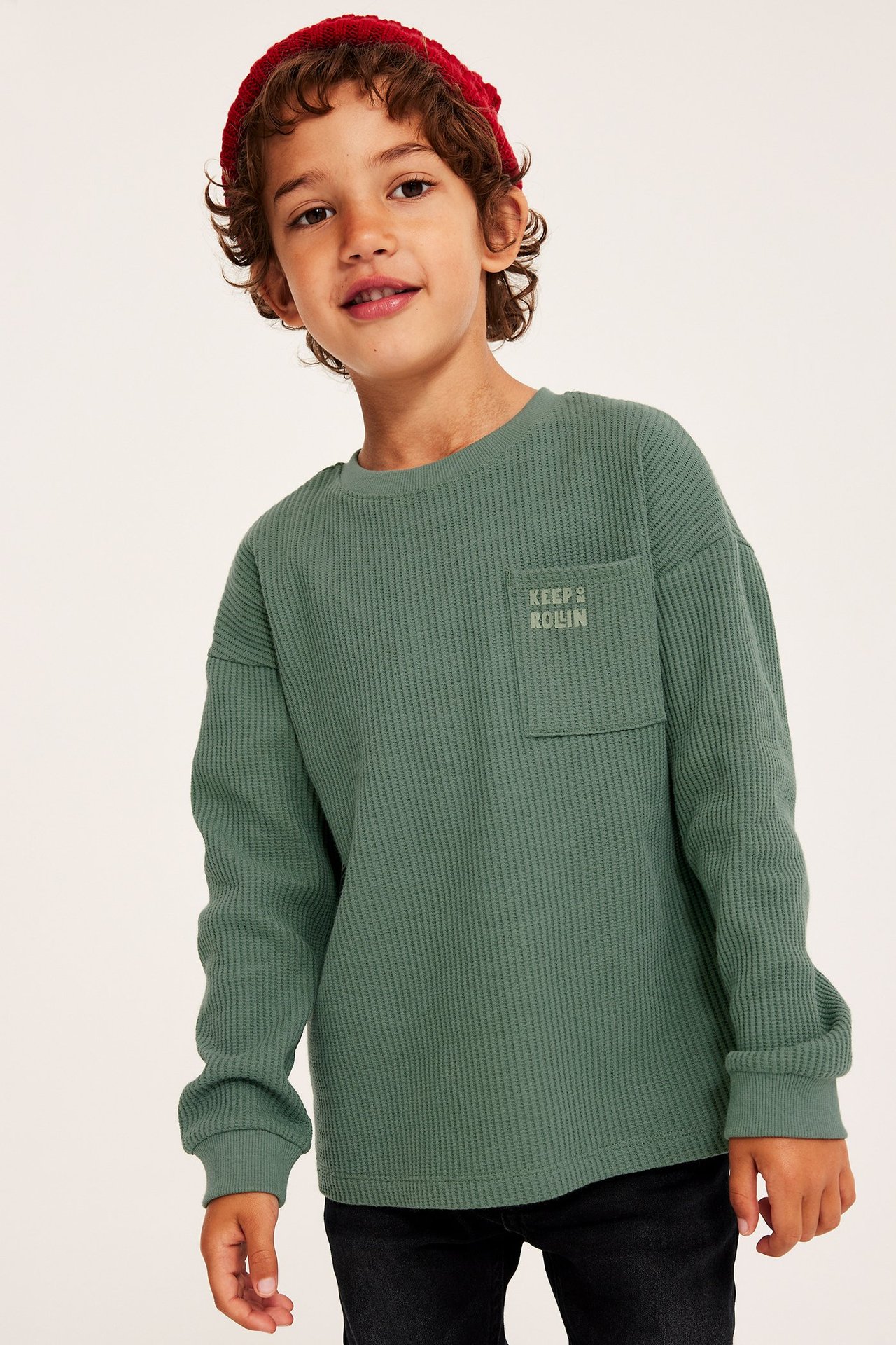 Widok z przodu: Dziecko w ciemnozielonej, waflowej koszulce z długim rękawem, kieszenią, nadrukiem i czerwoną czapką.
