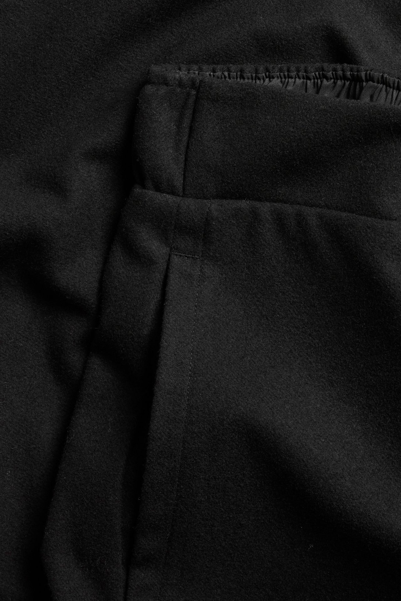 Zbliżenie na czarne, melanżowe spodnie z mieszanki wełny z elastycznym pasem i kieszenią boczną.