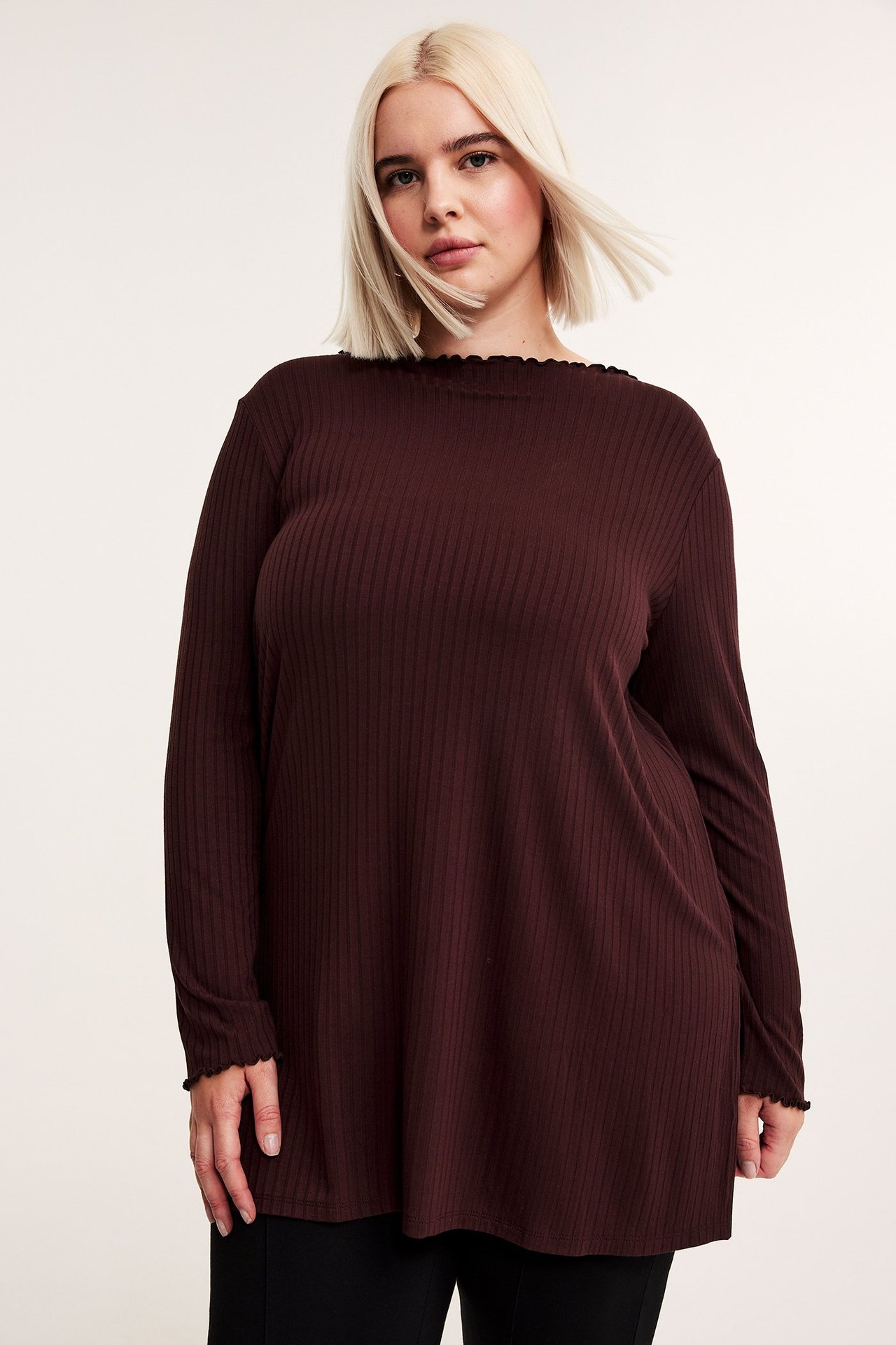 Widok z przodu: kobieta w bordowej prążkowanej tunice z falbankami i czarnych spodniach.