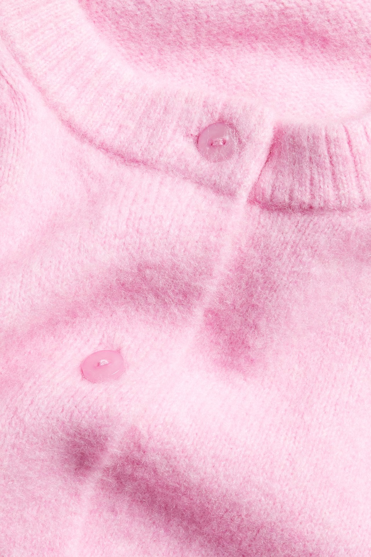 Zbliżenie różowego dzianinowego kardiganu z krótkim rękawem, okrągłym dekoltem i dwoma pasującymi guzikami.