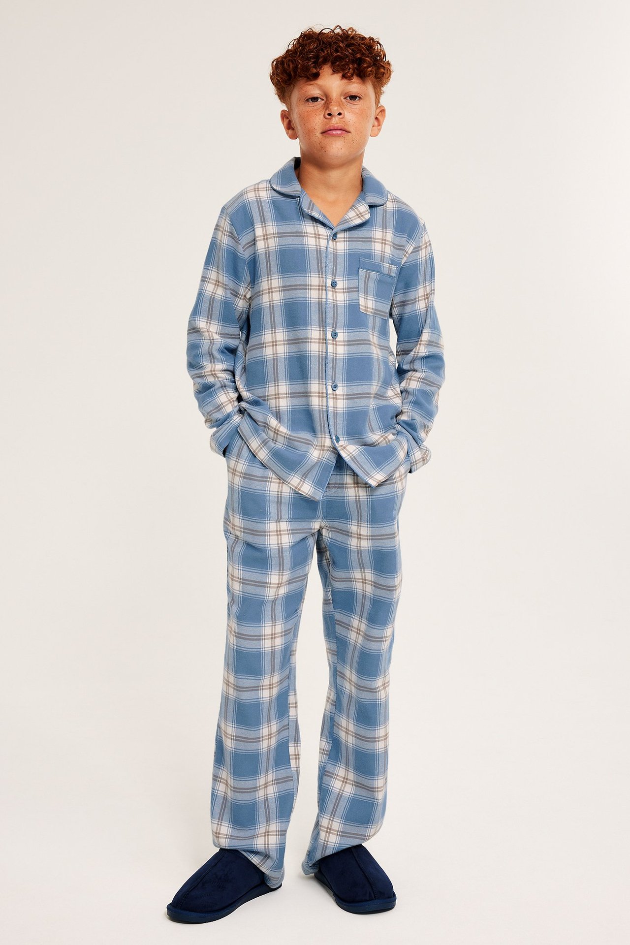 Dziecko w niebieskiej kratowanej piżamie flanelowej z guzikami, kieszeniami, prostymi nogawkami.