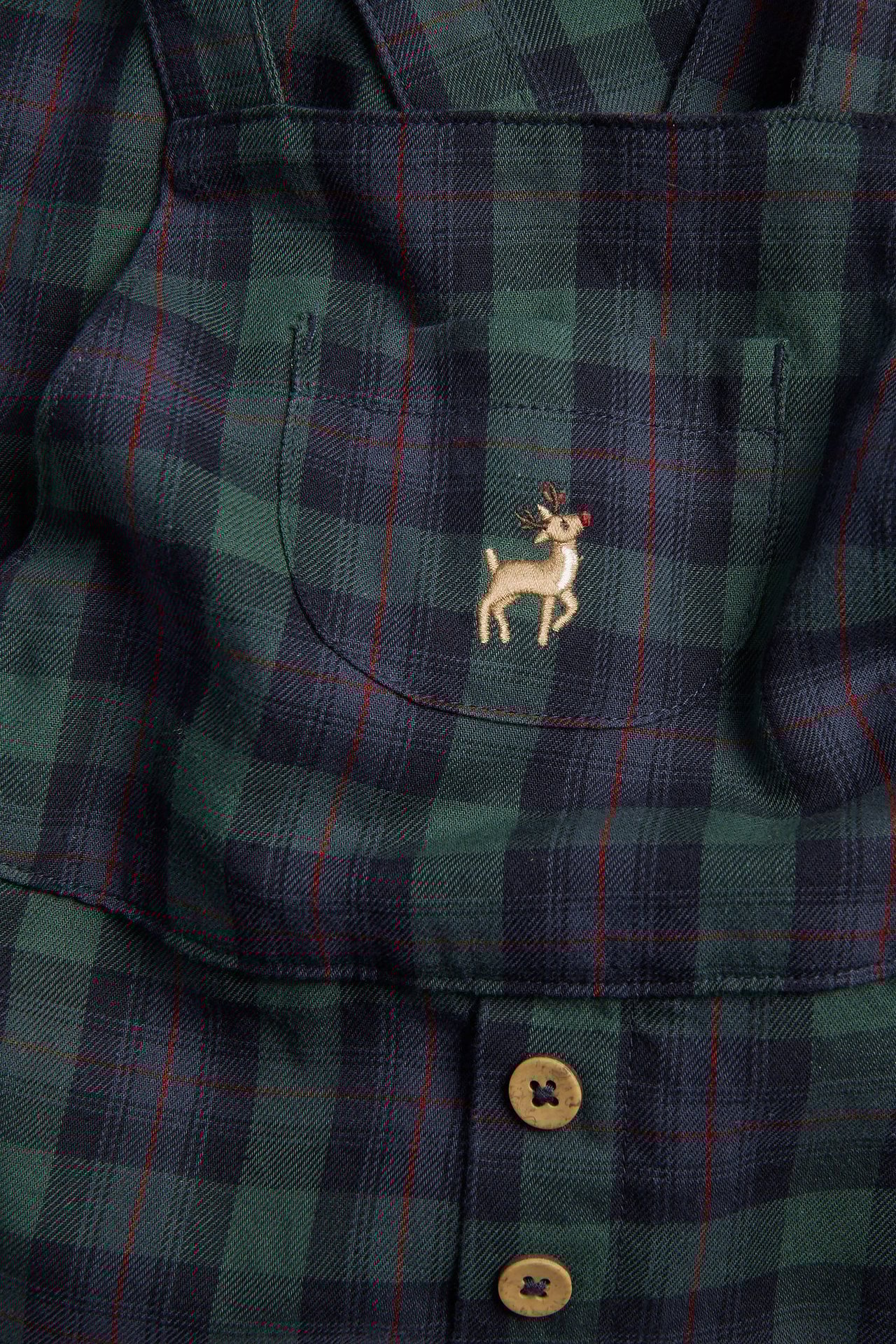 Zbliżenie: Dziecięce niebiesko-zielone bawełniane ogrodniczki w kratę, z reniferem i guzikami.