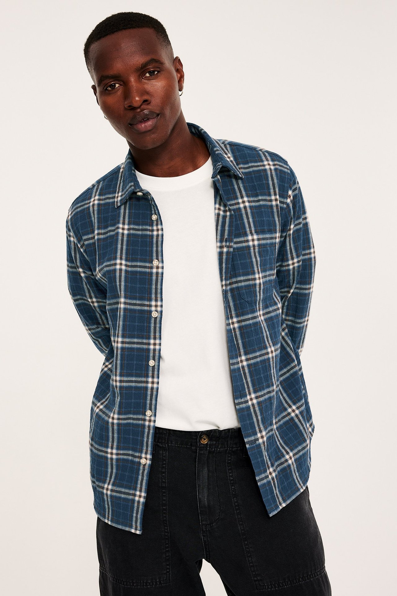Framifrån: man i öppen mörkblå rutig bomullsskjorta över vit t-shirt och mörka byxor.