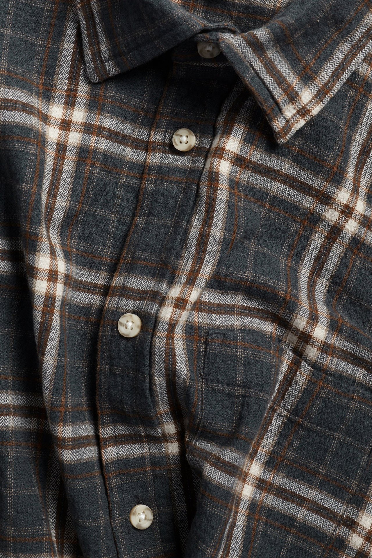 Zbliżenie z przodu męskiej, ciemnoszarej, białej, brązowej koszuli bawełnianej w kratę z guzikami i kieszenią.