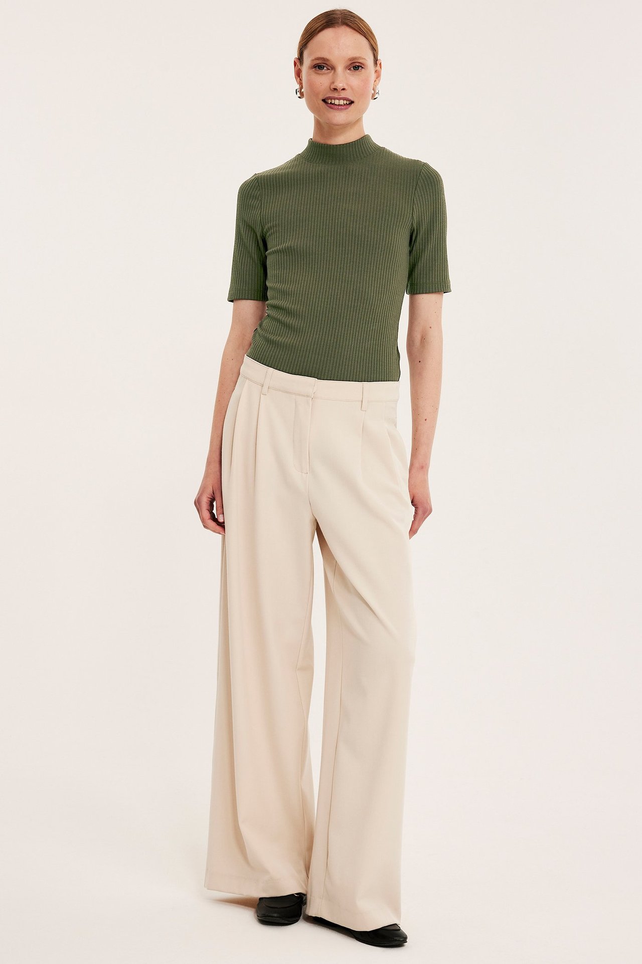 Widok z przodu: kobieta w zielonym prążkowanym topie polo z krótkim rękawem i beżowych szerokich spodniach.