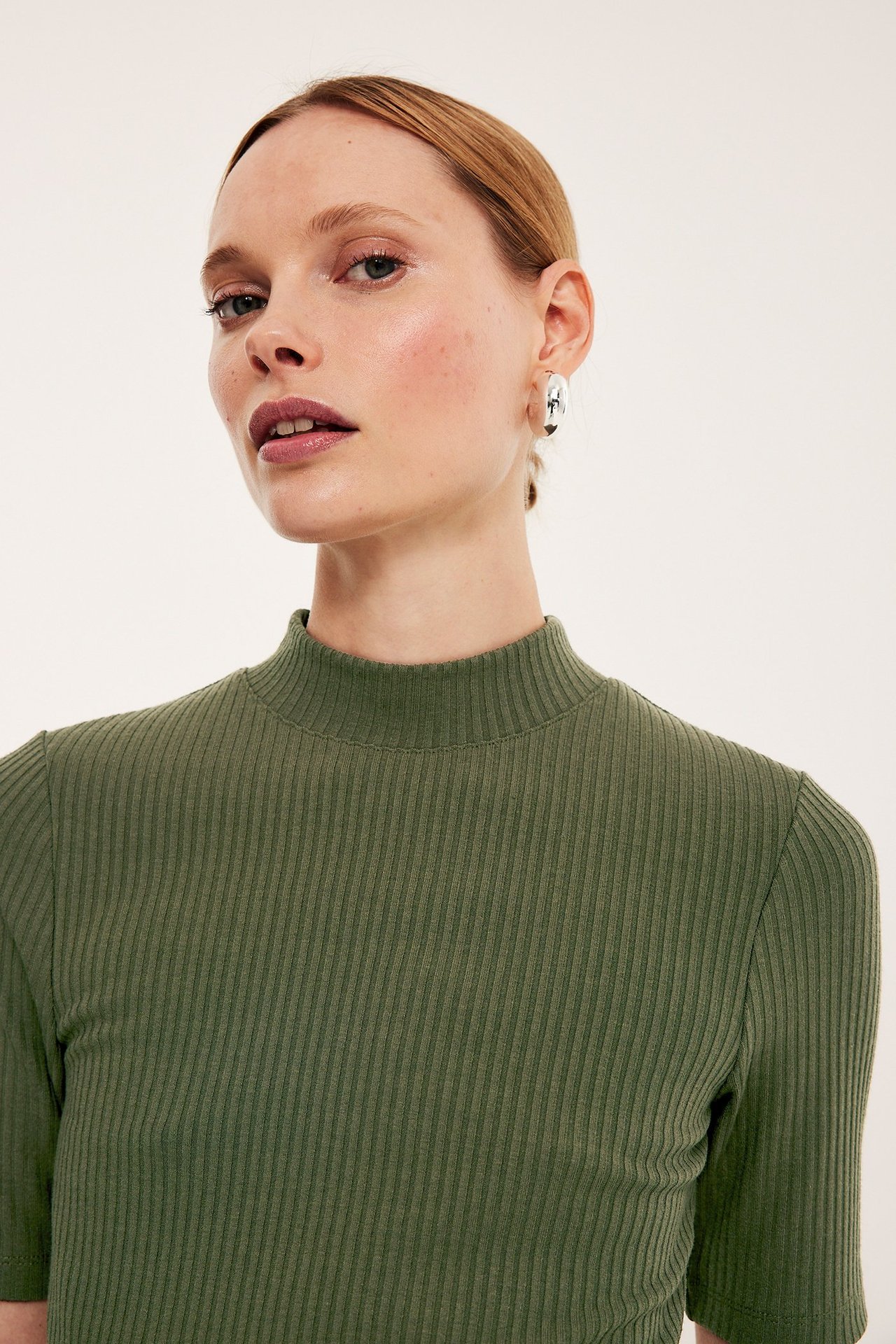 Zbliżenie z przodu kobiety w zielonym prążkowanym topie polo z krótkim rękawem i srebrnych kolczykach.