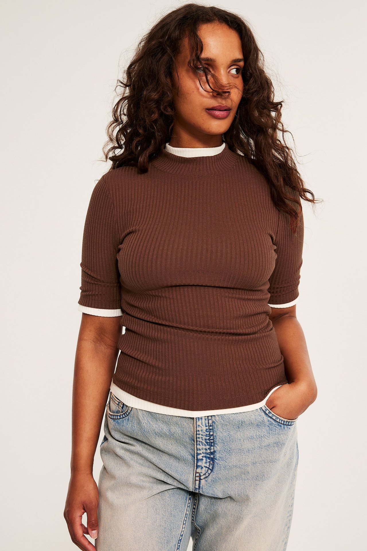 Widok z przodu: Kobieta w brązowym prążkowanym topie polo z krótkim rękawem, na białej warstwie, z jasnych dżinsach.