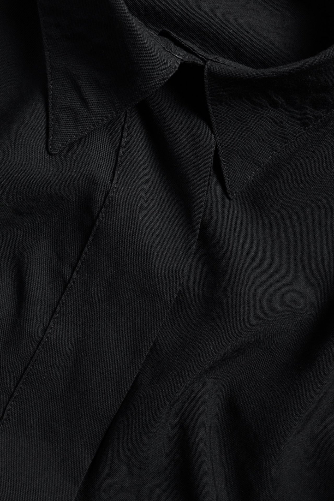 Zbliżenie czarnej, oversize'owej koszuli z mieszanki wiskozy z kołnierzykiem i ukrytym zapięciem.