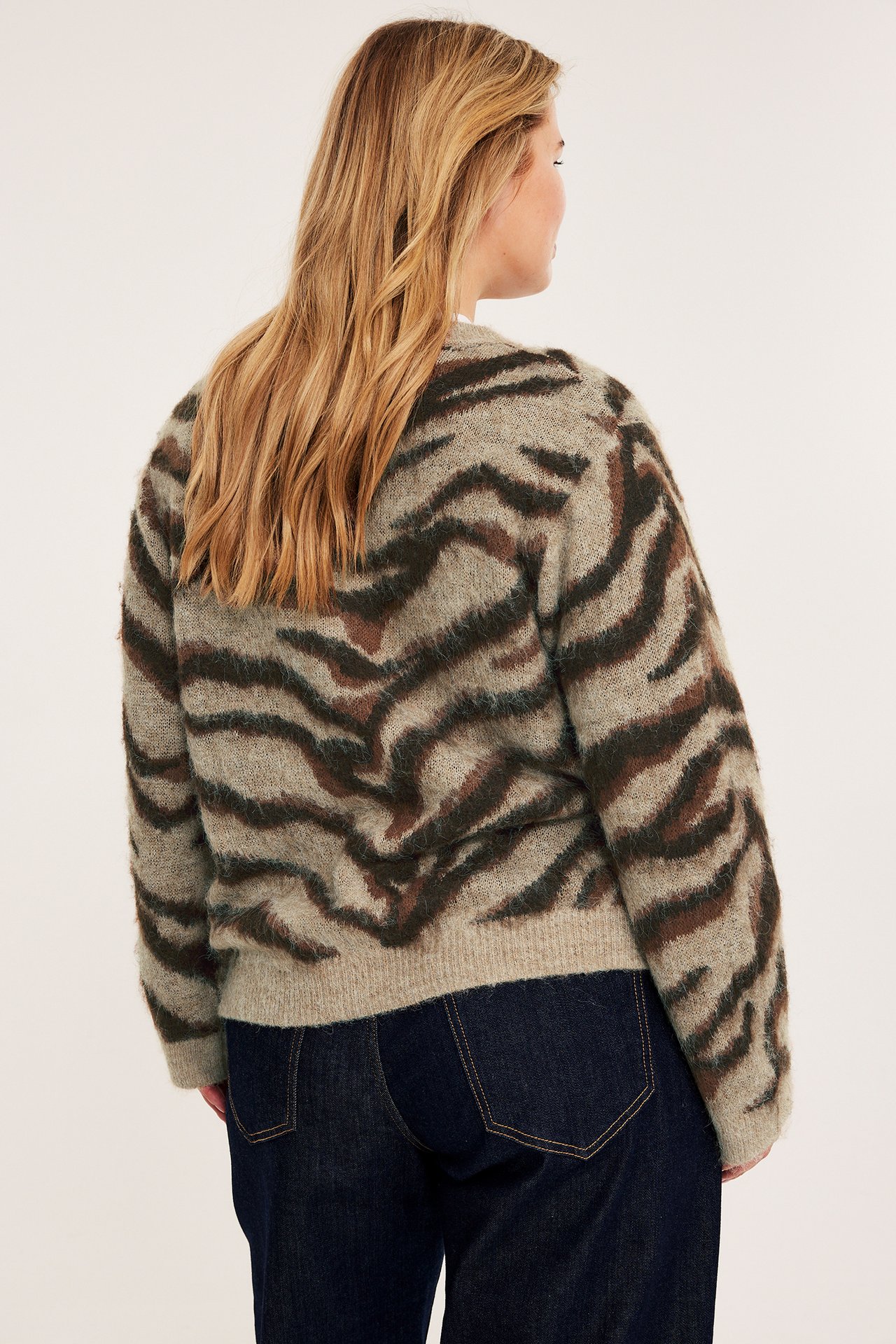 Bakfra av en kvinne i en beige tigermønstret lodden genser og mørkeblå jeans.