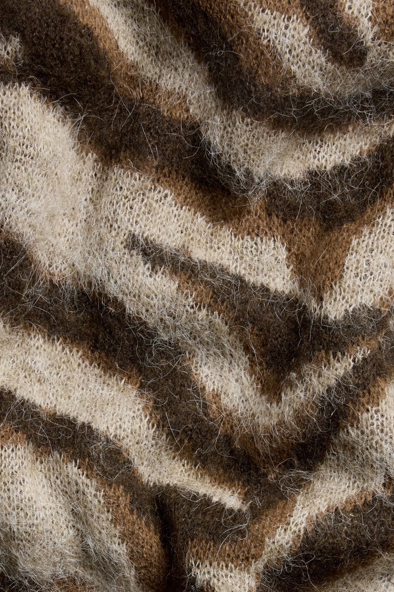 Nærbilde av et beige, brunt og mørkebrunt fluffy strikket stoff med tigermønster fra en genser.