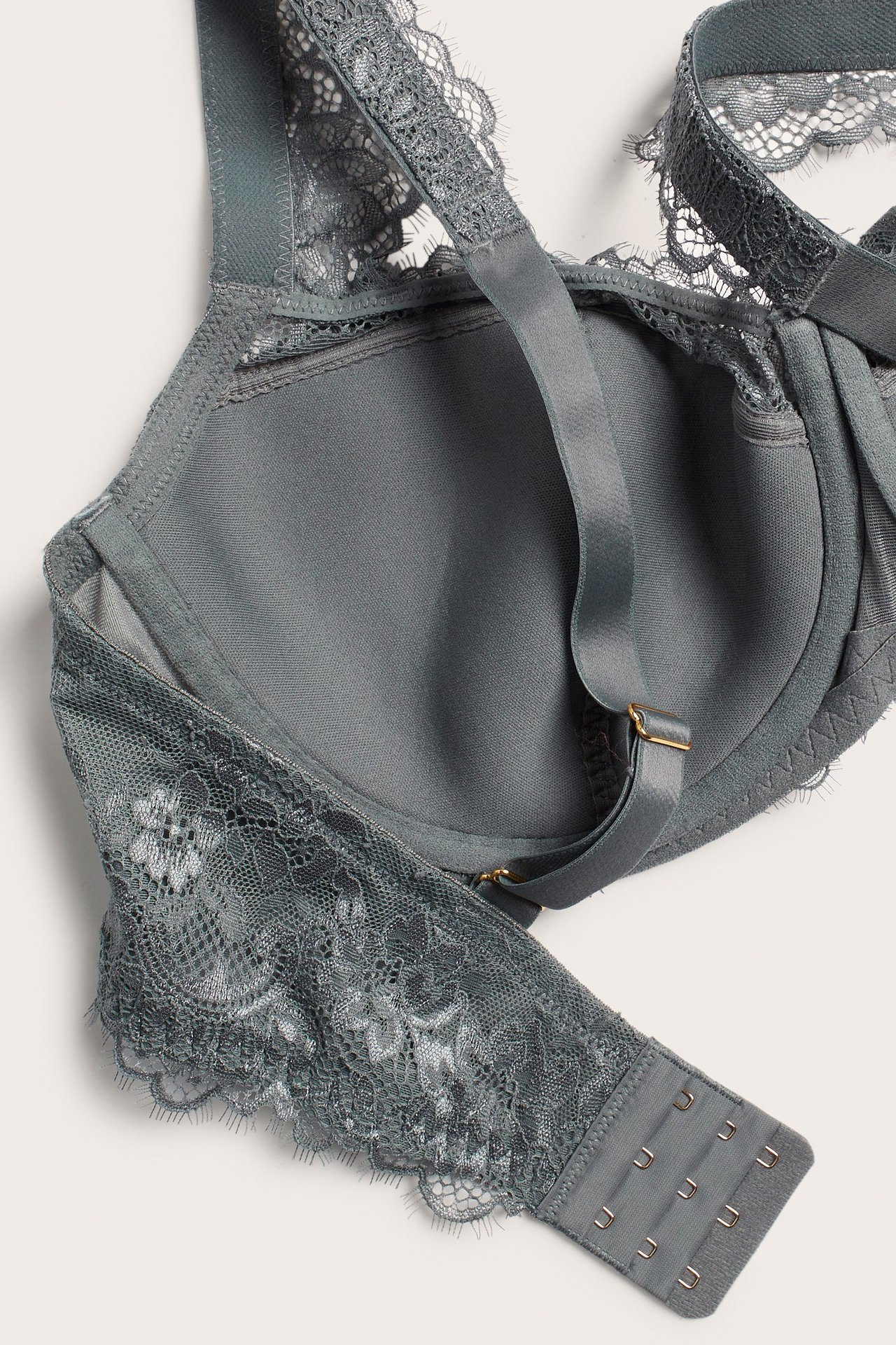 Zbliżenie szarego koronkowego biustonosza typu balconette z miękką półfiliżankową wyściółką, regulowanymi ramiączkami i zapięciem na haftki.