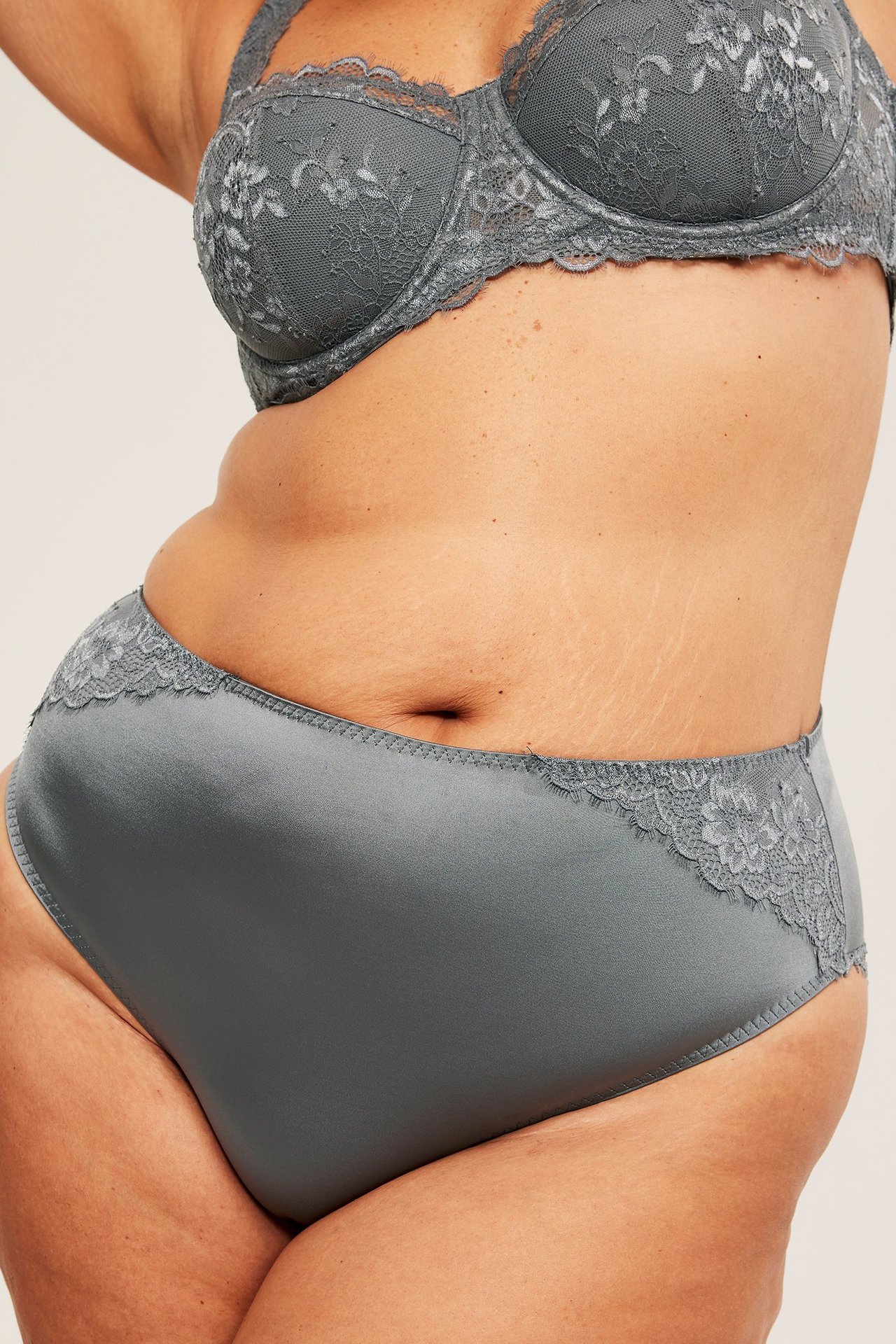 Sivukuva naisesta harmaissa satiinipikkuhousuissa pitsireunuksella ja yhteensopivissa pitsiliiveissä.