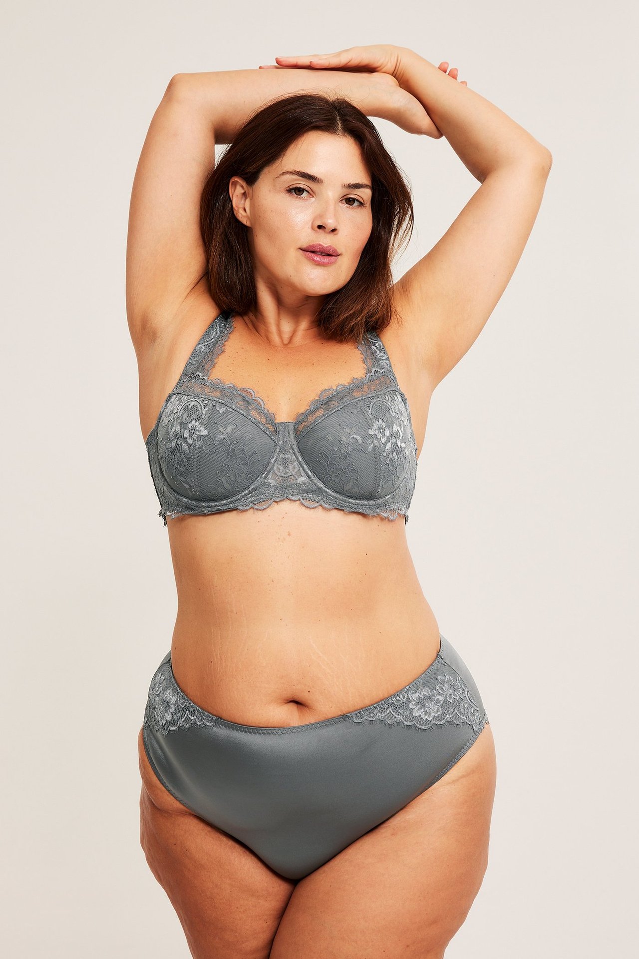 Forfra: en kvinne i grå tøyelige satengtruser med blondekanter og en matchende grå blonde-BH.