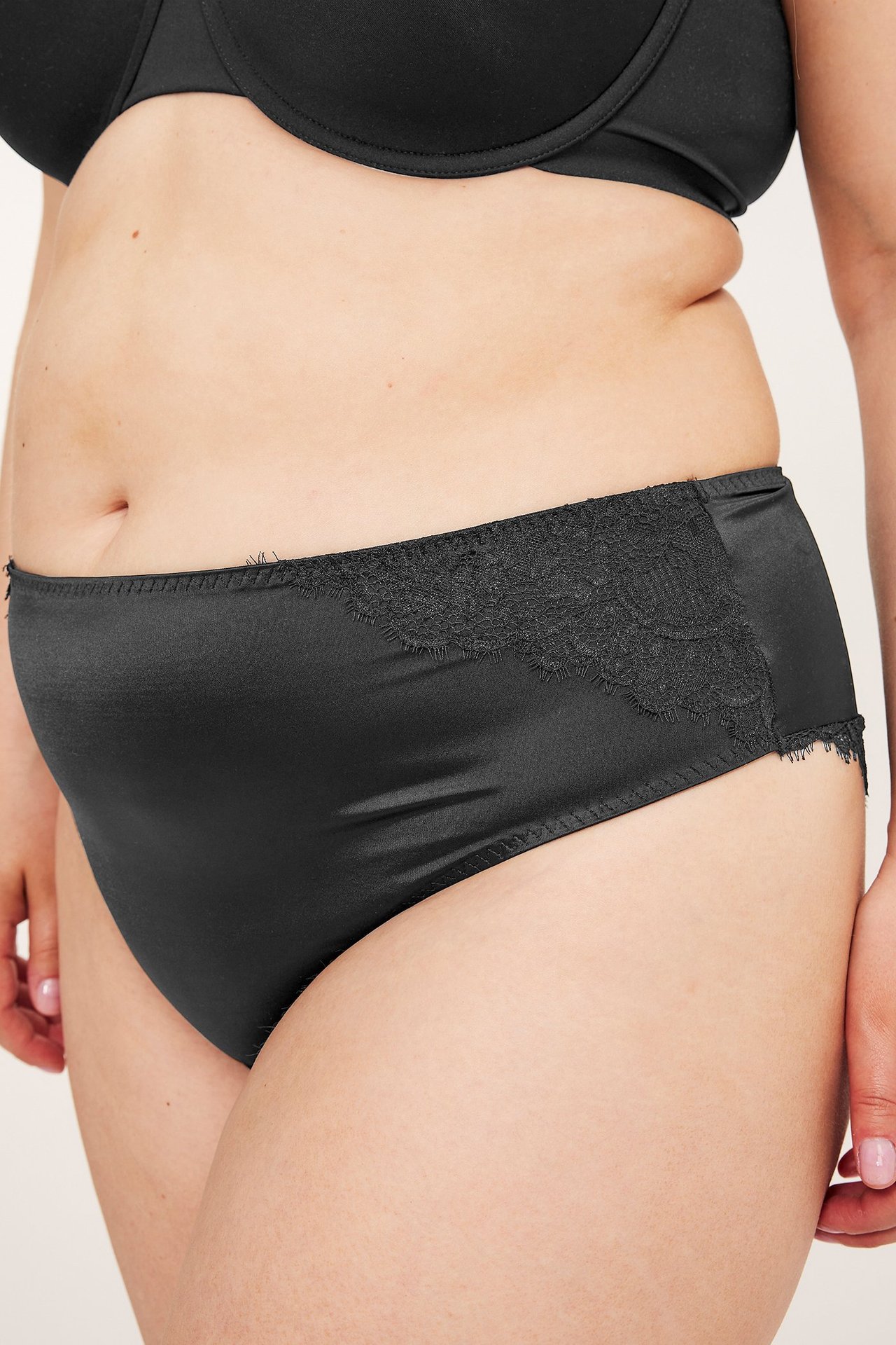 Lähikuva naisen sivusta mustissa, joustavissa satiinimikro cheeky-alushousuissa pitsiyksityiskohdilla ja mustissa rintaliiveissä.