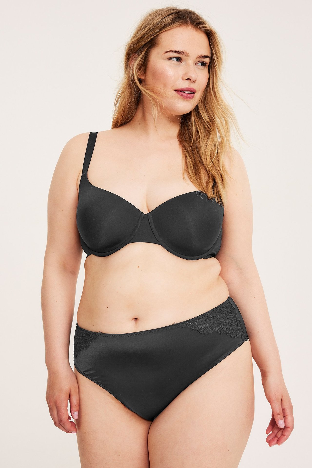 Frontutsikt av kvinne i svarte satin mikro truser med blonde, matchende med en svart BH.