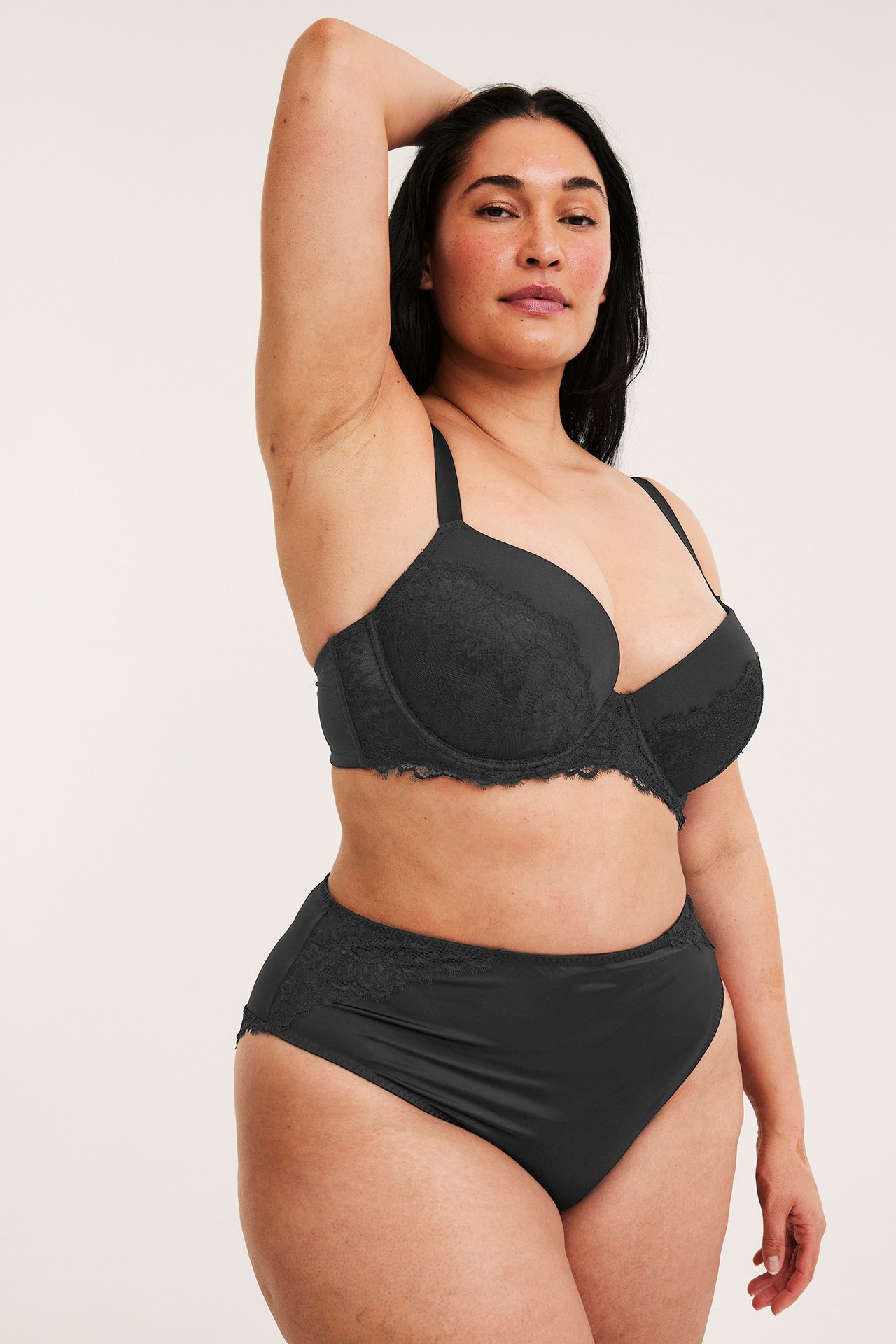 Frontvy av en kvinna i svarta satin micro cheeky trosor med spetskant och matchande svart spetsbehå.