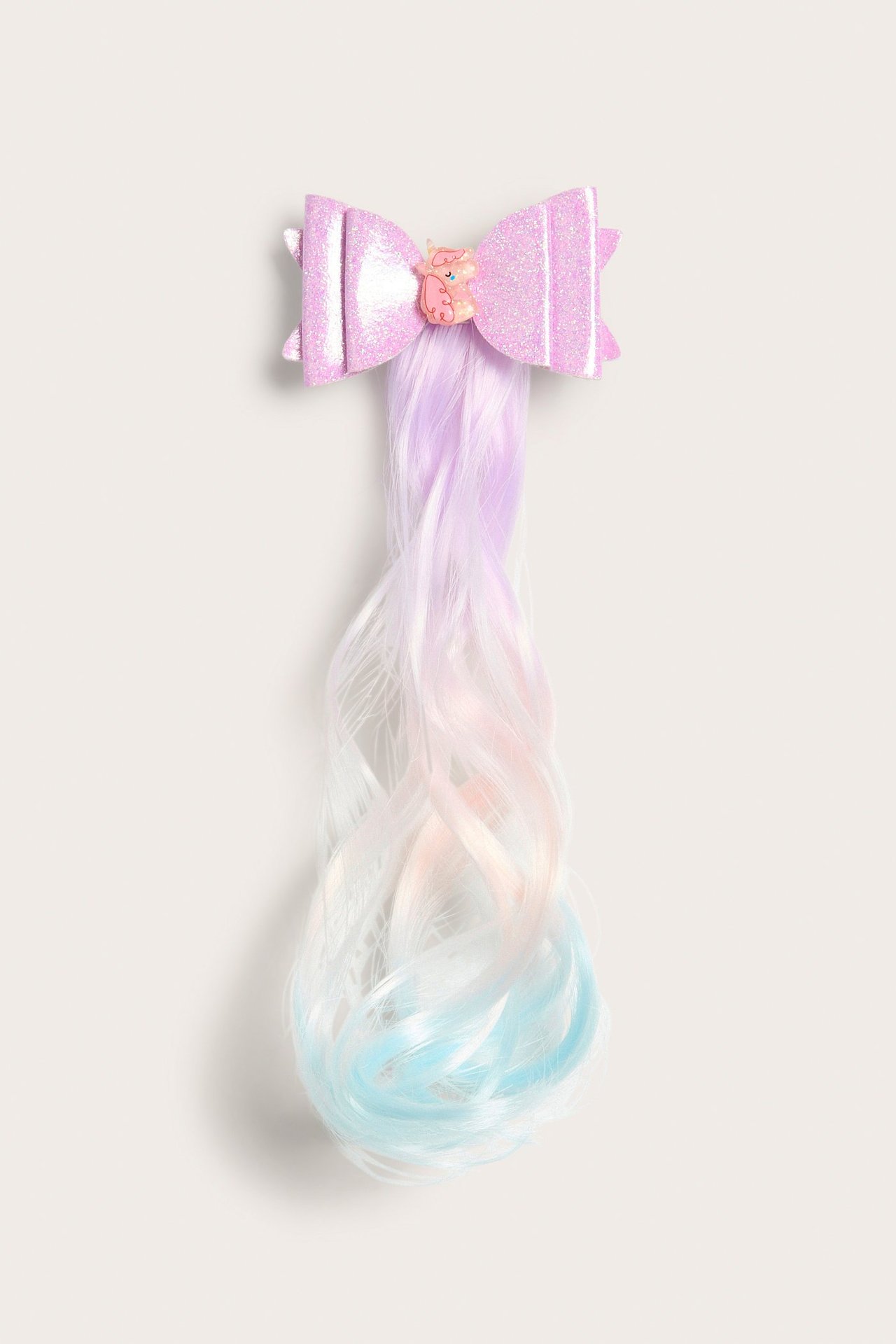 Edestä näkymä lasten kimaltelevaan vaaleanpunaiseen rusettihiusklipsiin, jossa yksisarvinen ja pitkät sateenkaarihiukset.