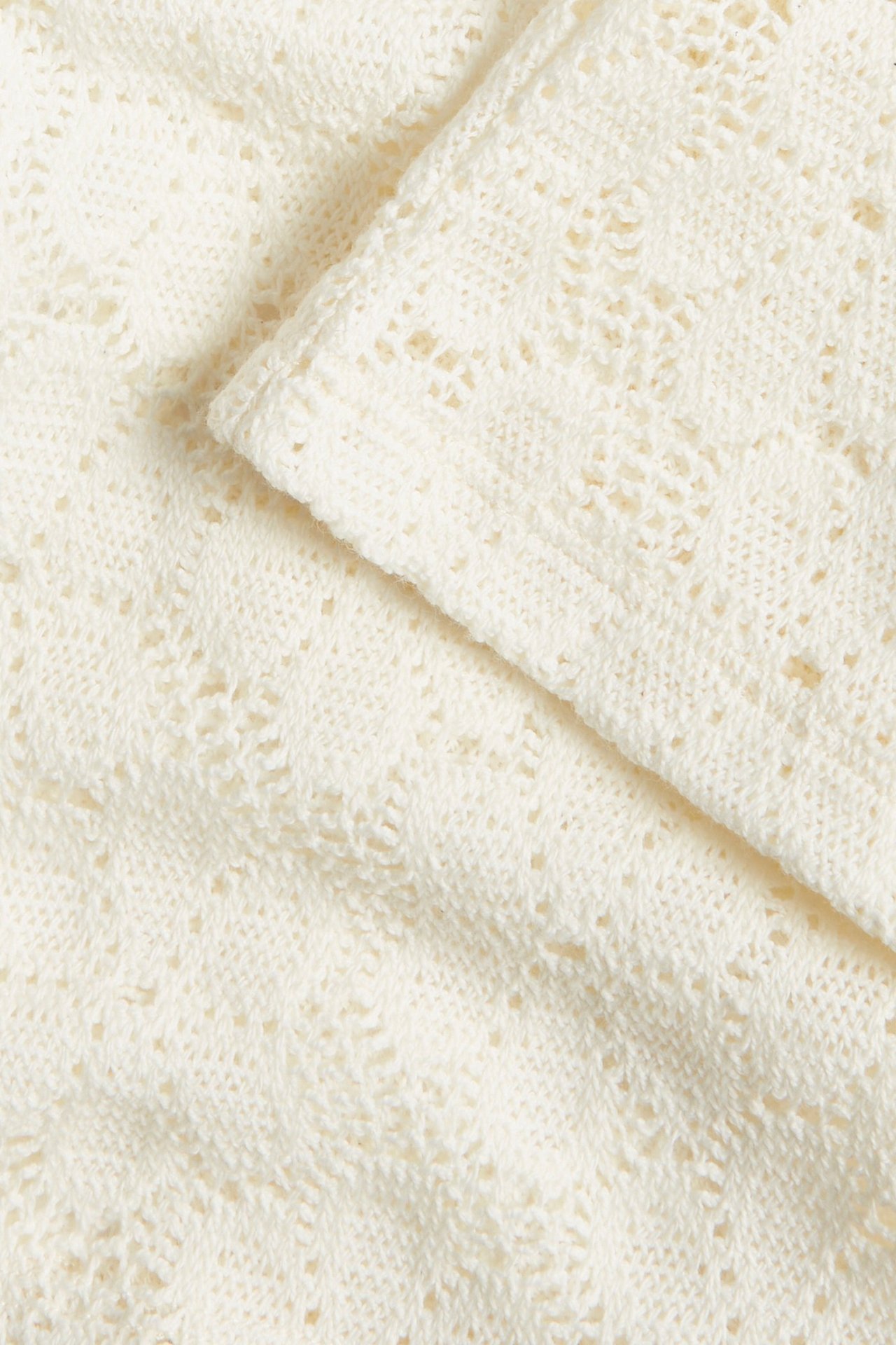 Zbliżenie na tkaninę rozkloszowanych spodni z koronki w kolorze ecru z delikatnym wzorem.