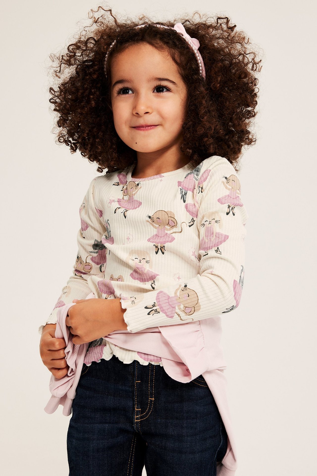 Barns framifrån: ribbad off-white långärmad topp med djurmönster, mörka jeans, rosa diadem.